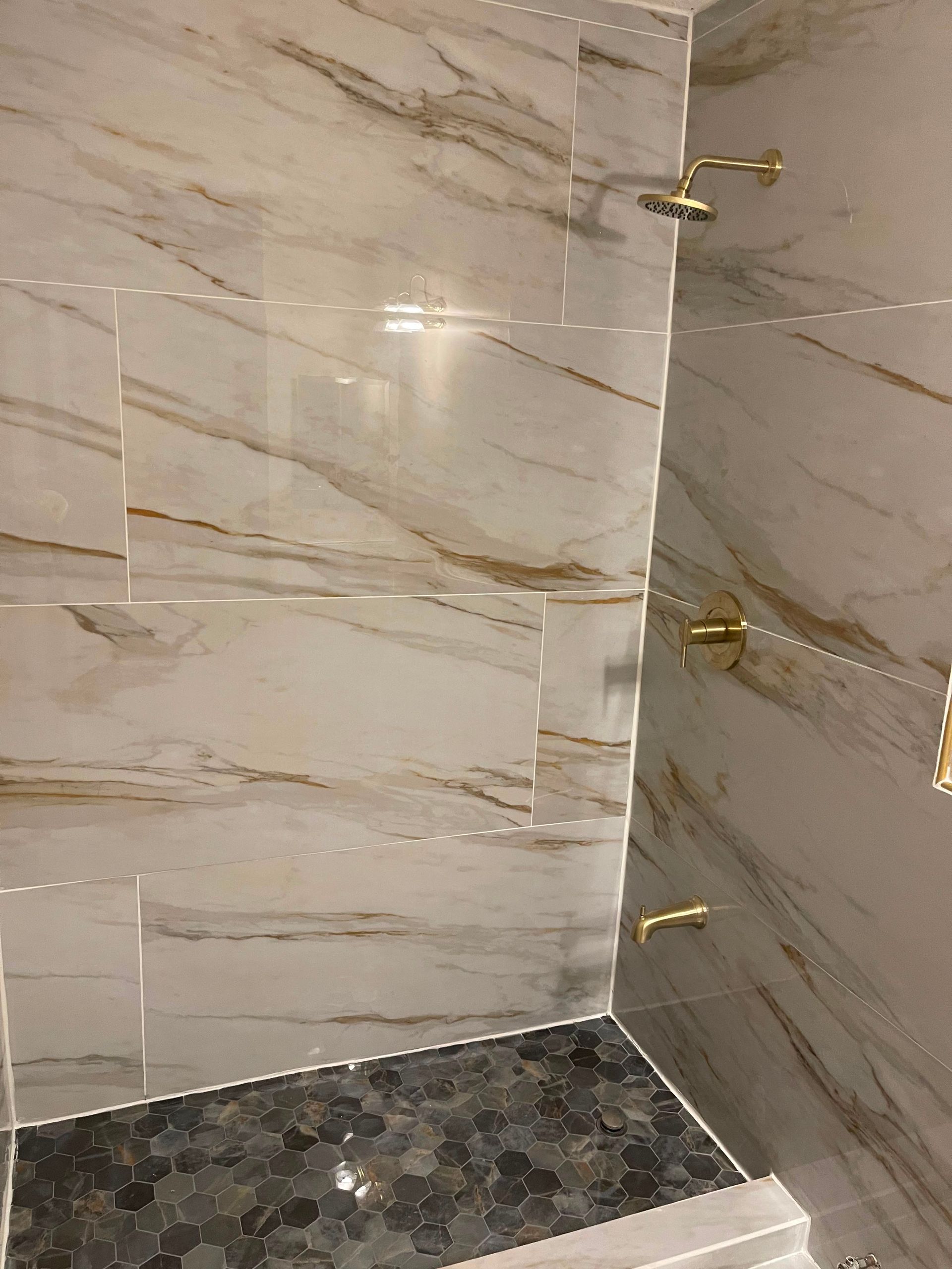 Marble-tiled shower corner with dark stone floor and two wall-mounted brass fixtures