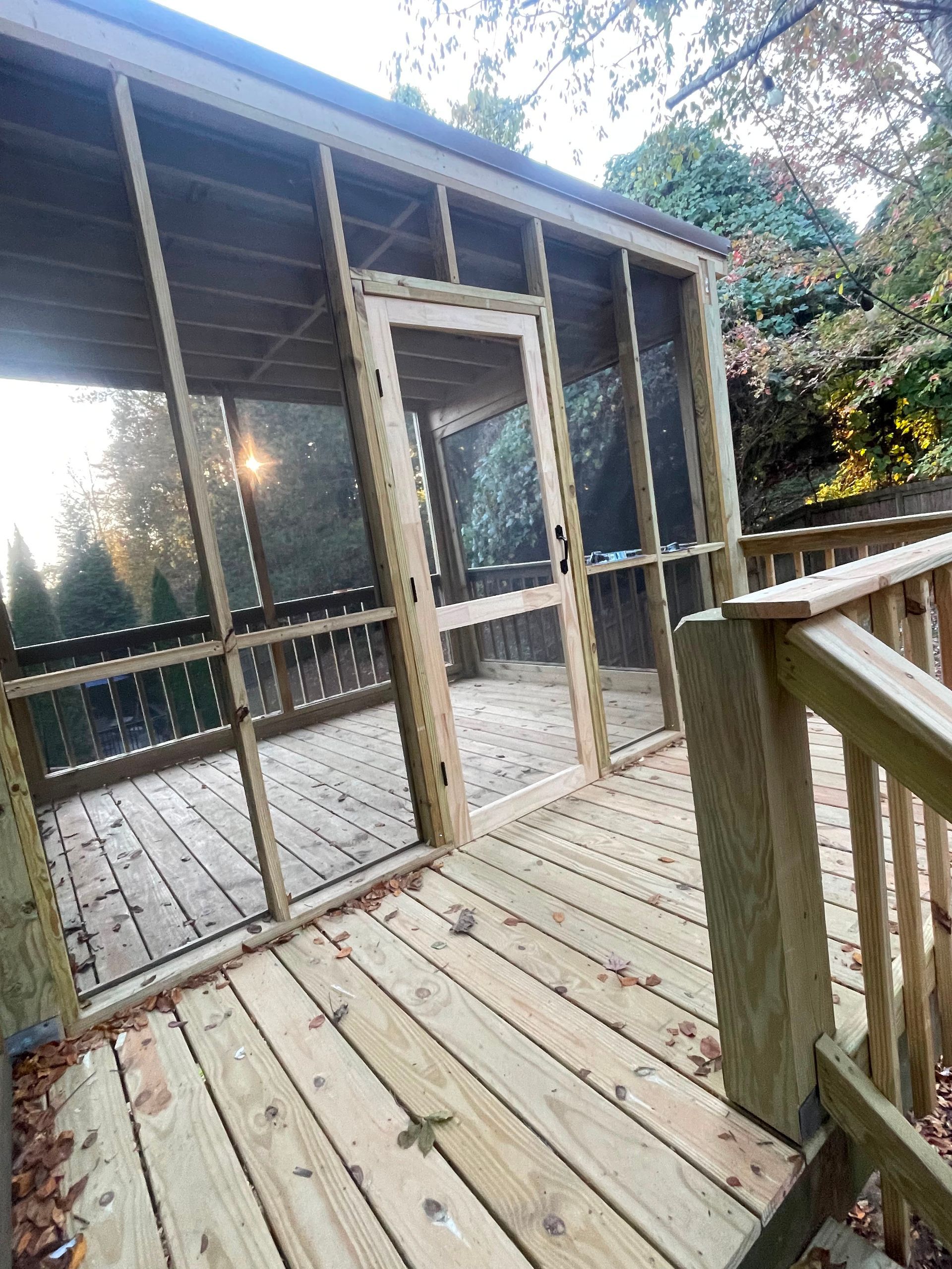 Wooden deck and screened porch with stairs and railing in a wooded backyard.