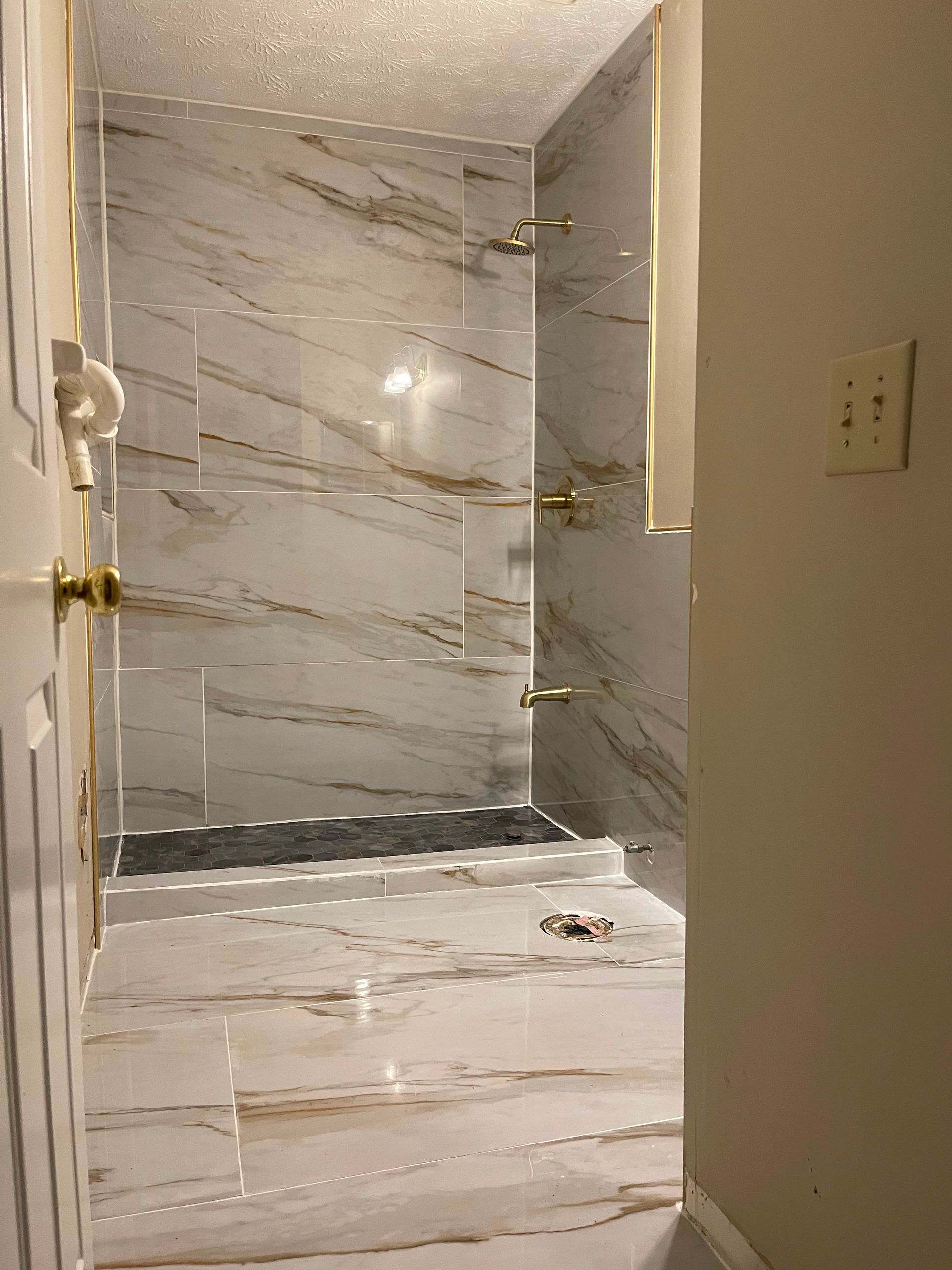 Modern bathroom with marble-tiled shower and tub seen through an open doorway
