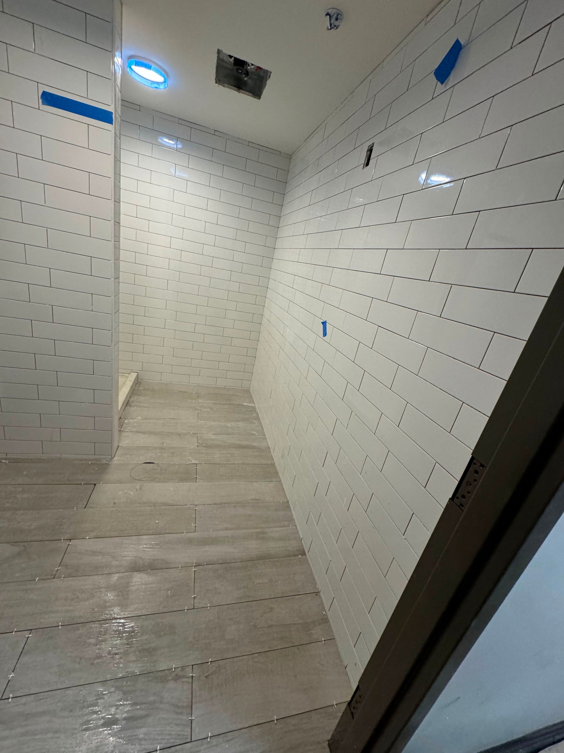 Narrow tiled shower room with white walls, light wood-look floor, and a ceiling light.