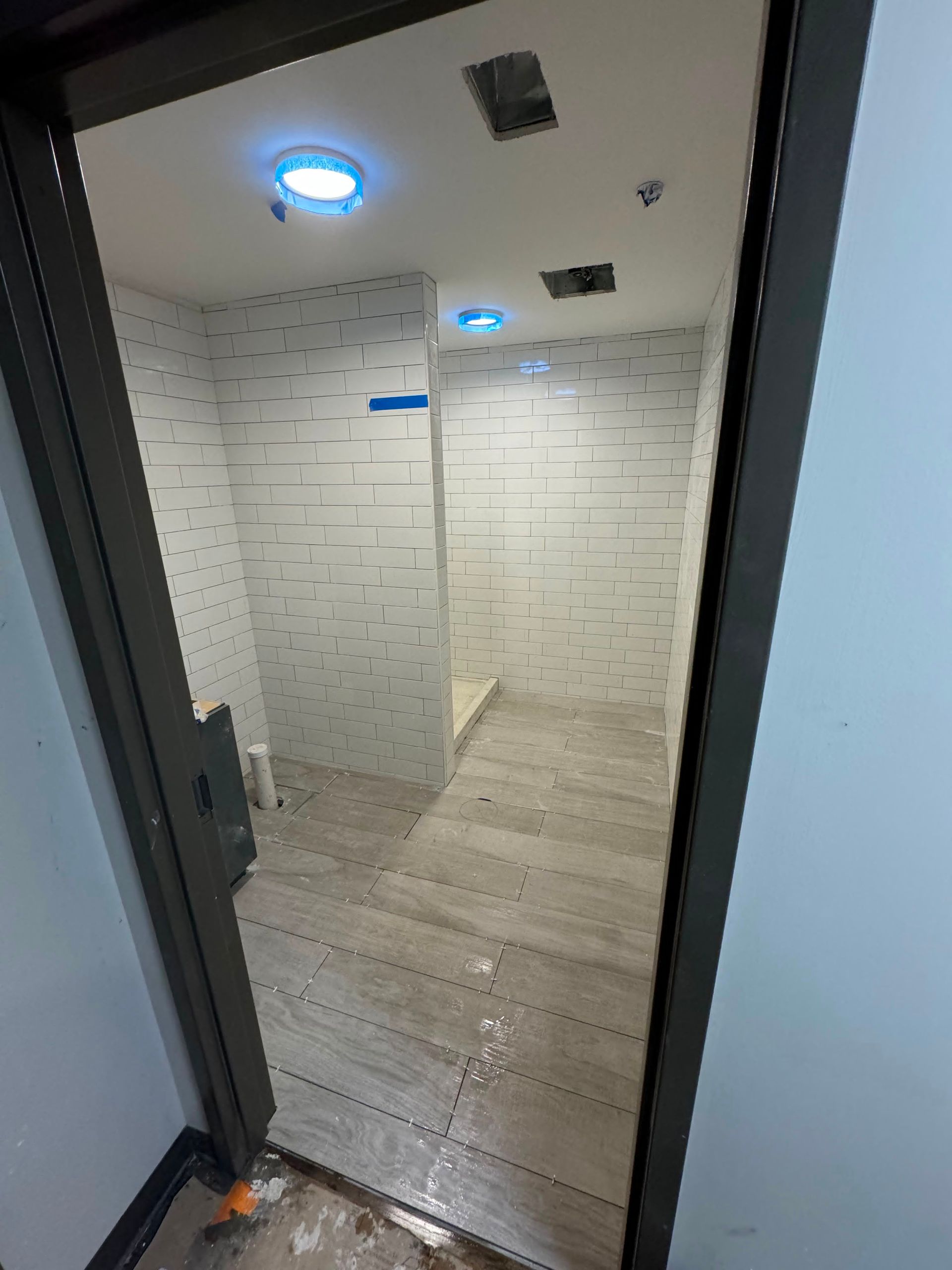 Small tiled restroom with two lit ceiling fixtures and a narrow doorway.