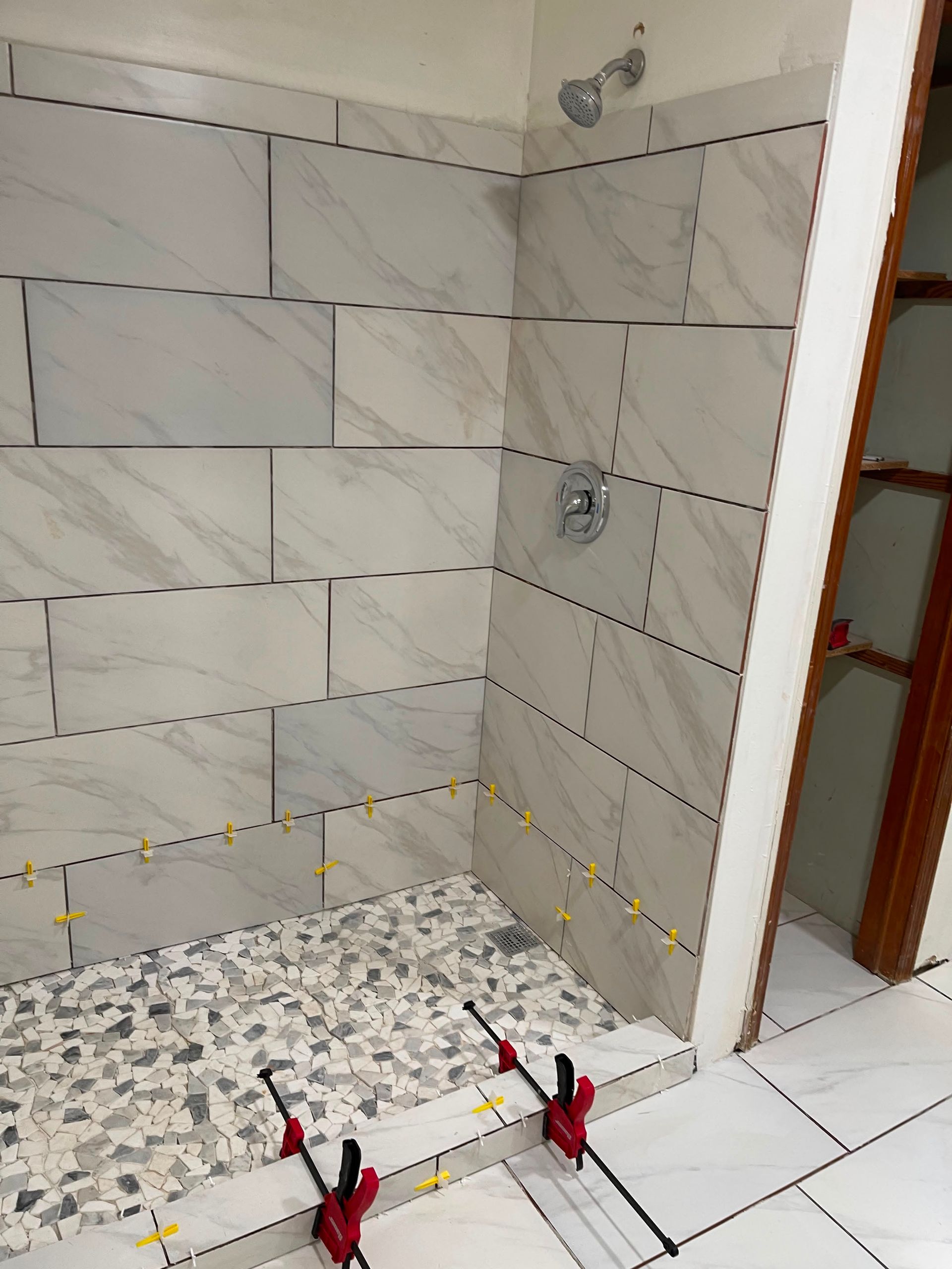 Partially tiled shower stall with speckled pebble floor and tile spacers near the threshold