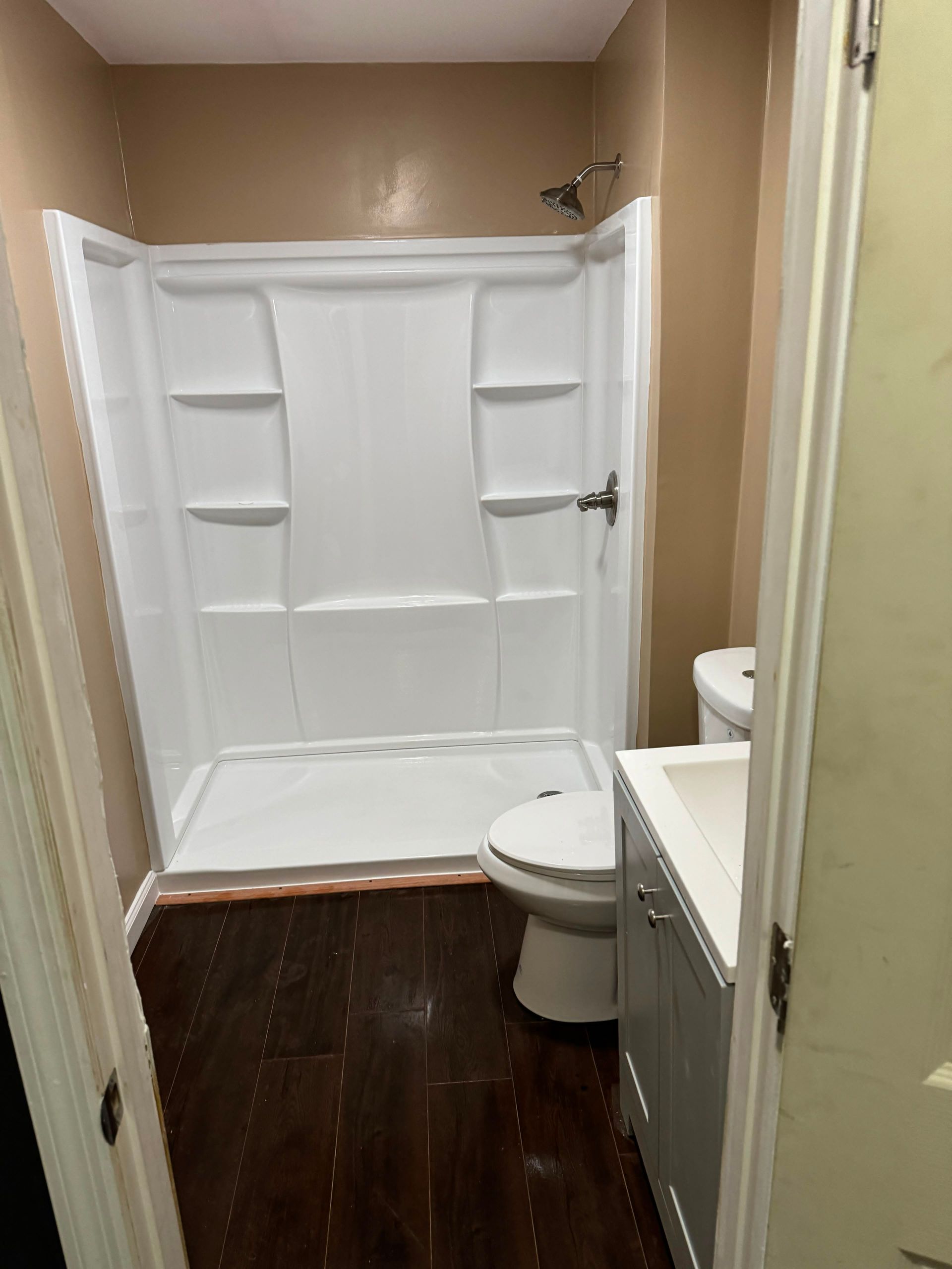 Small bathroom with white shower curtain, toilet, and dark wood floor.