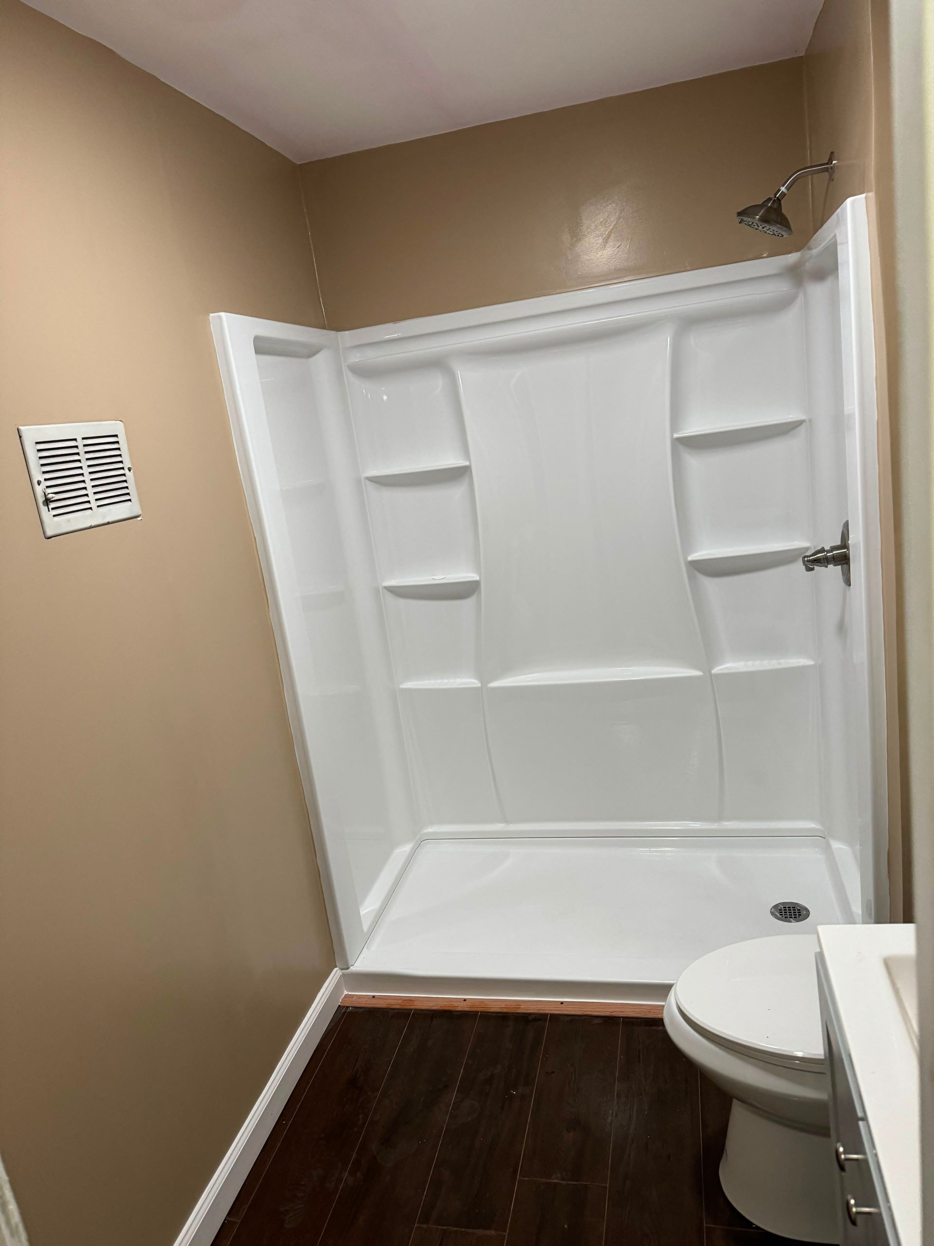 White walk-in shower with built-in shelves and toilet in a beige bathroom.