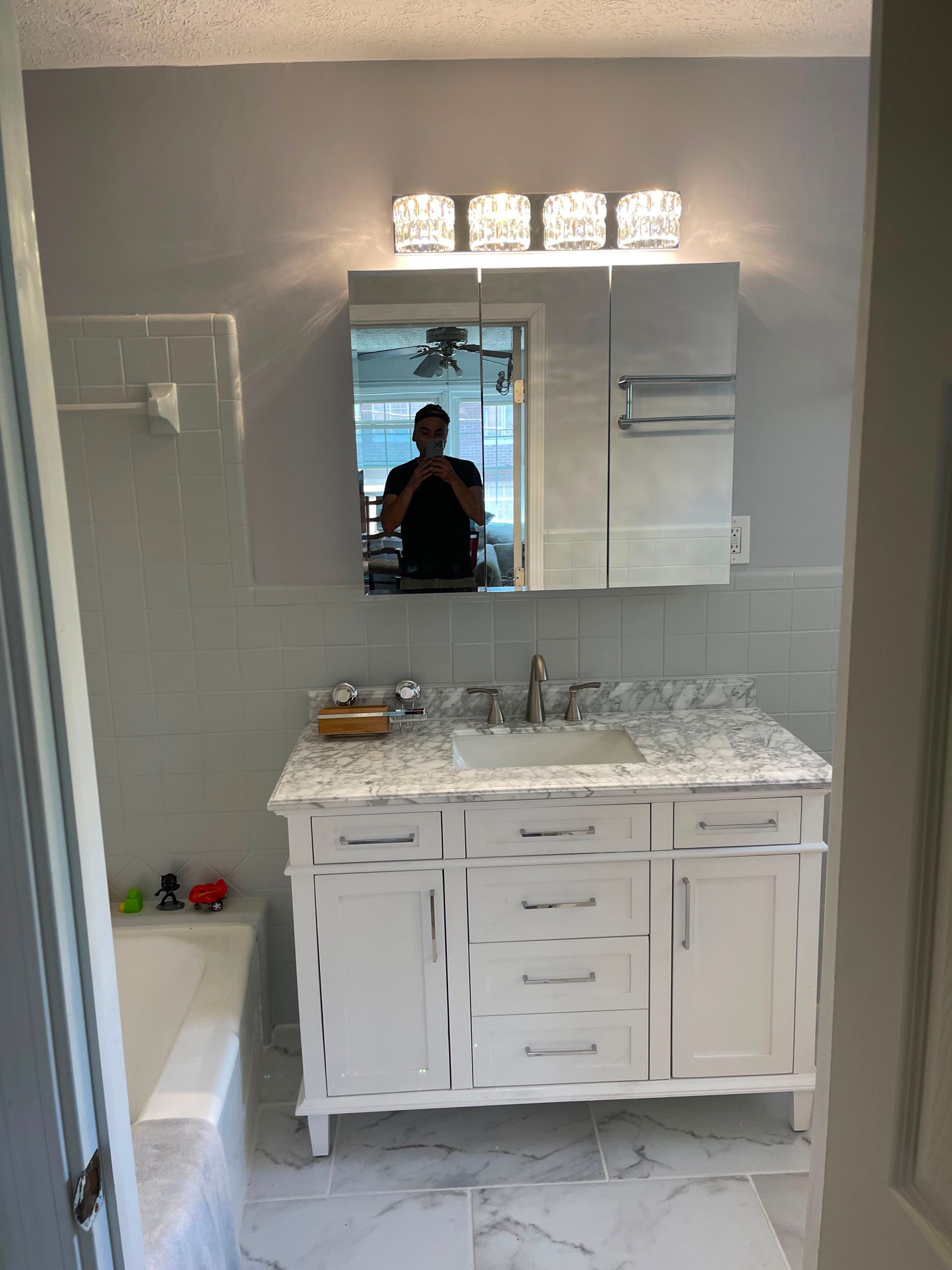 White bathroom vanity with sink, large mirror, and light fixture above a small doorway.