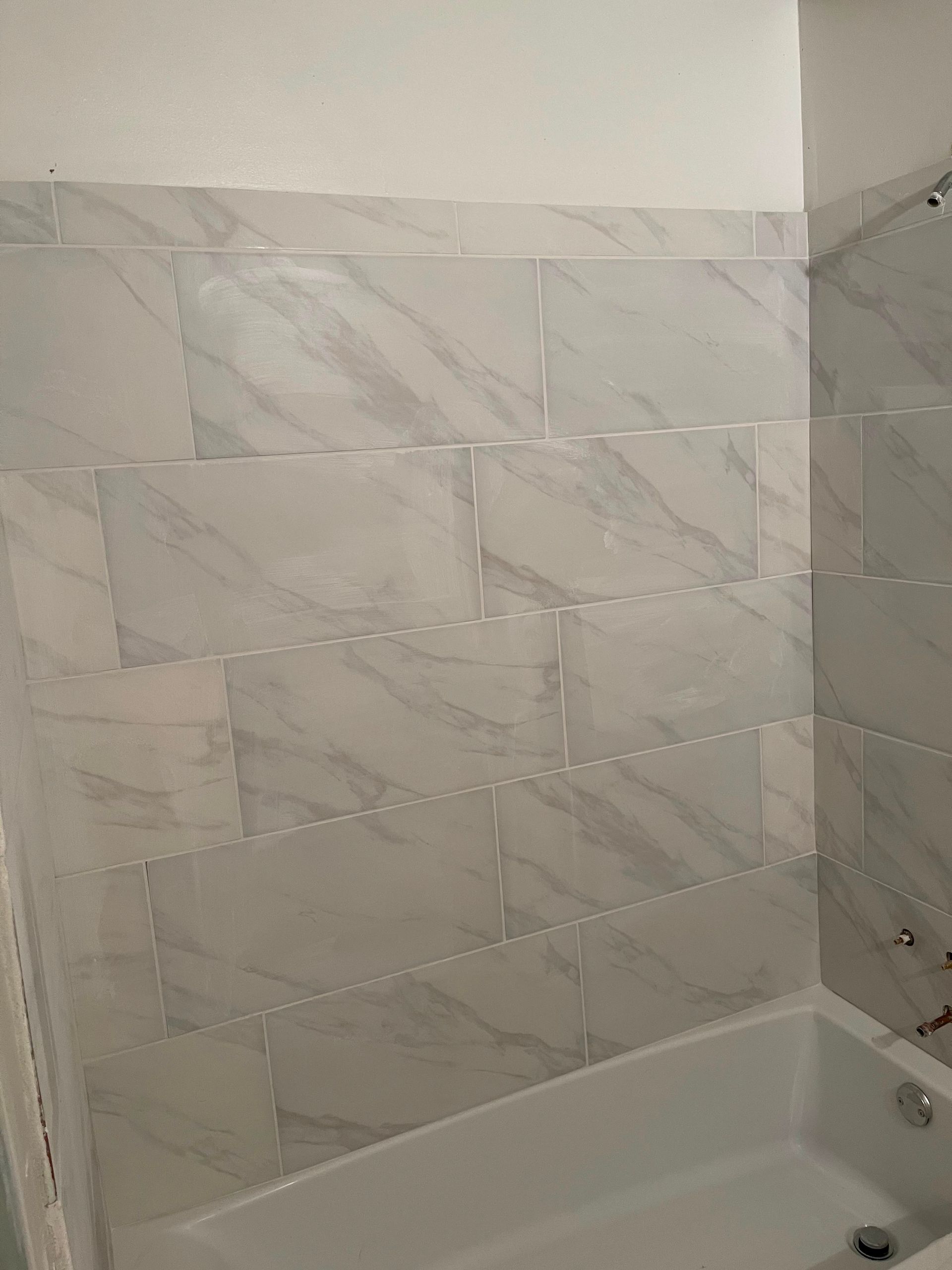 Tiled bathtub shower surround with white tub and gray marble-pattern wall tiles.