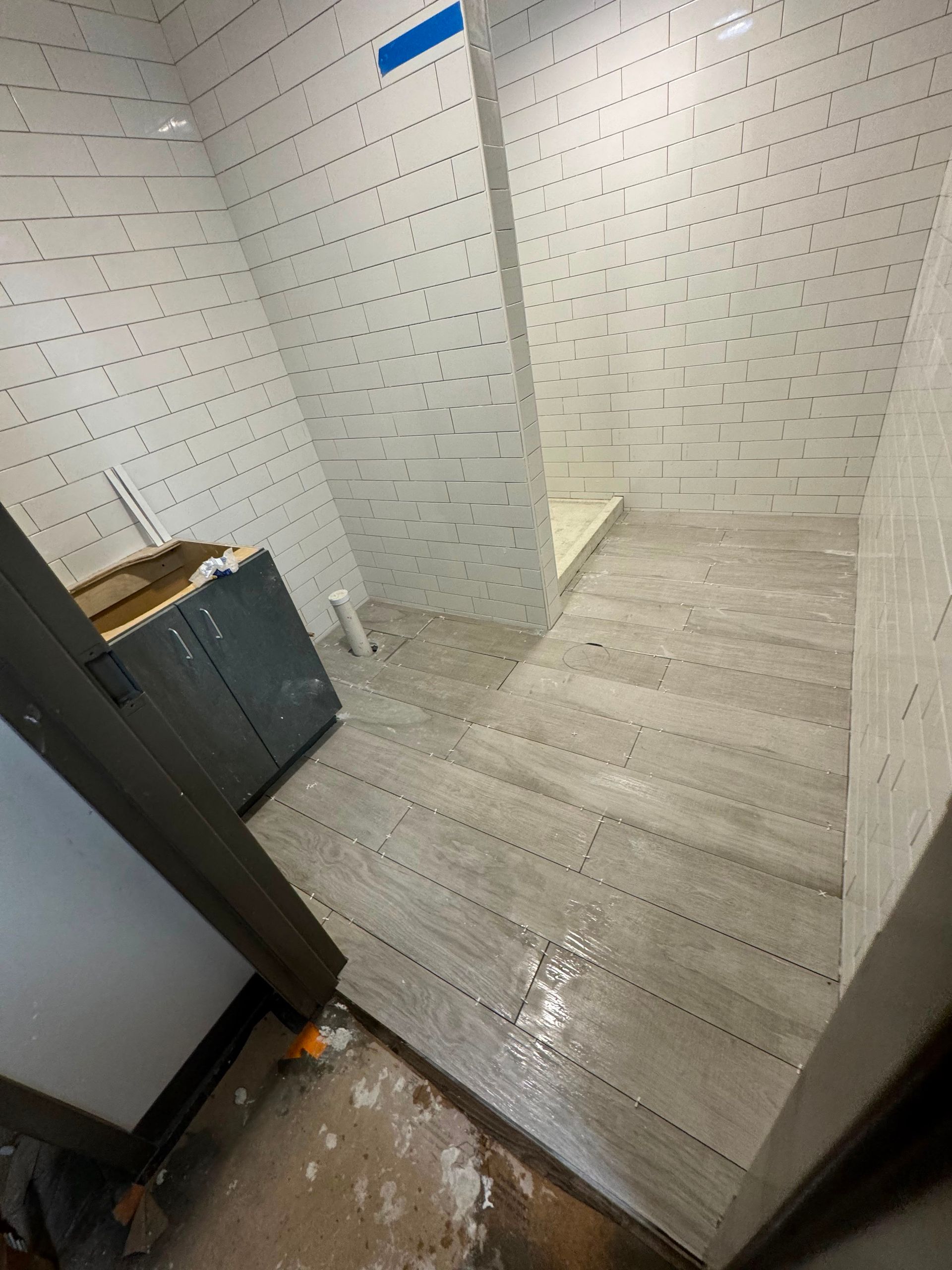 Empty restroom with white tiled walls, light wood-look floor, and a partial stall partition.