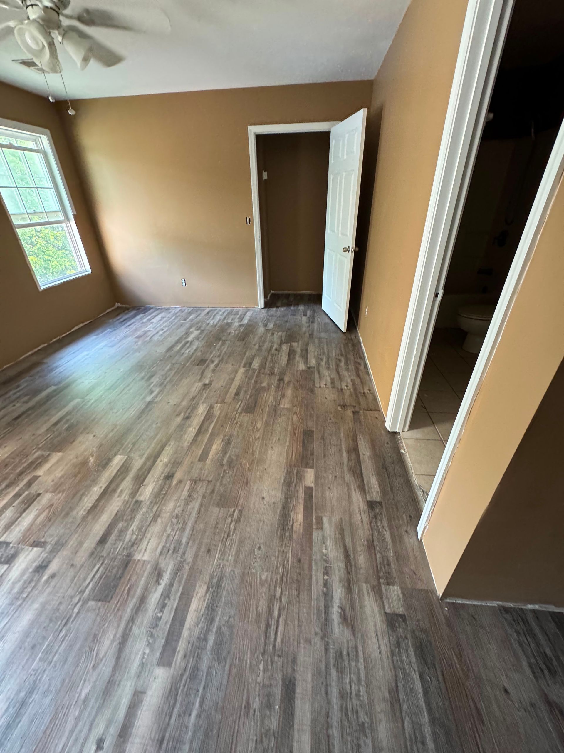 Empty room with wood-look flooring, tan walls, a window, and an open doorway.