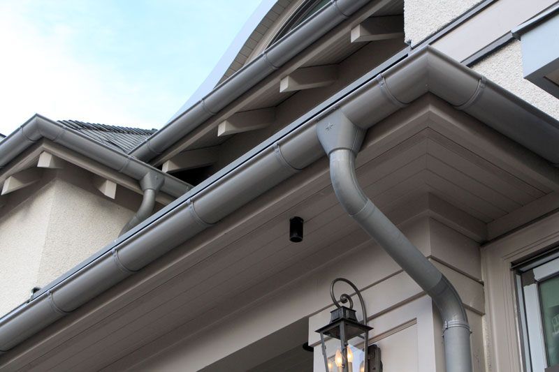 Close-up of a house eave with gray gutters, downspout, and a porch light under a tiled roof