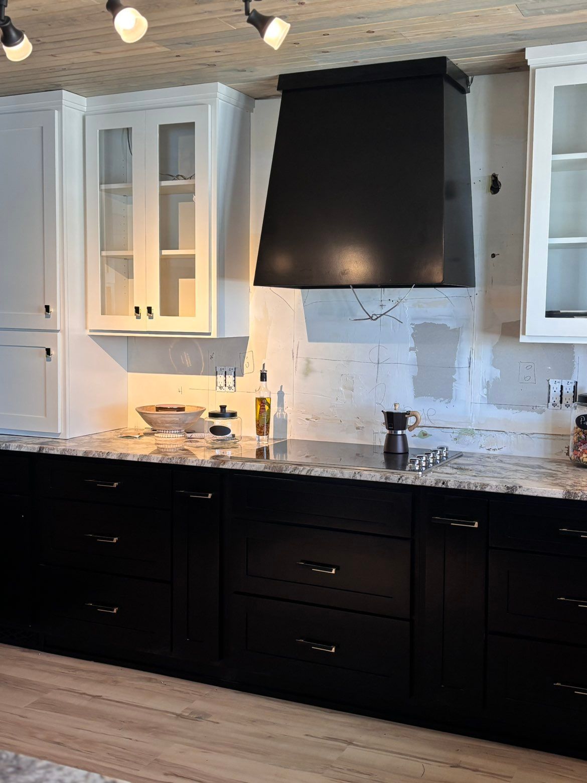 Modern kitchen with black cabinets, marble countertops, and white upper cabinets under a black range hood.