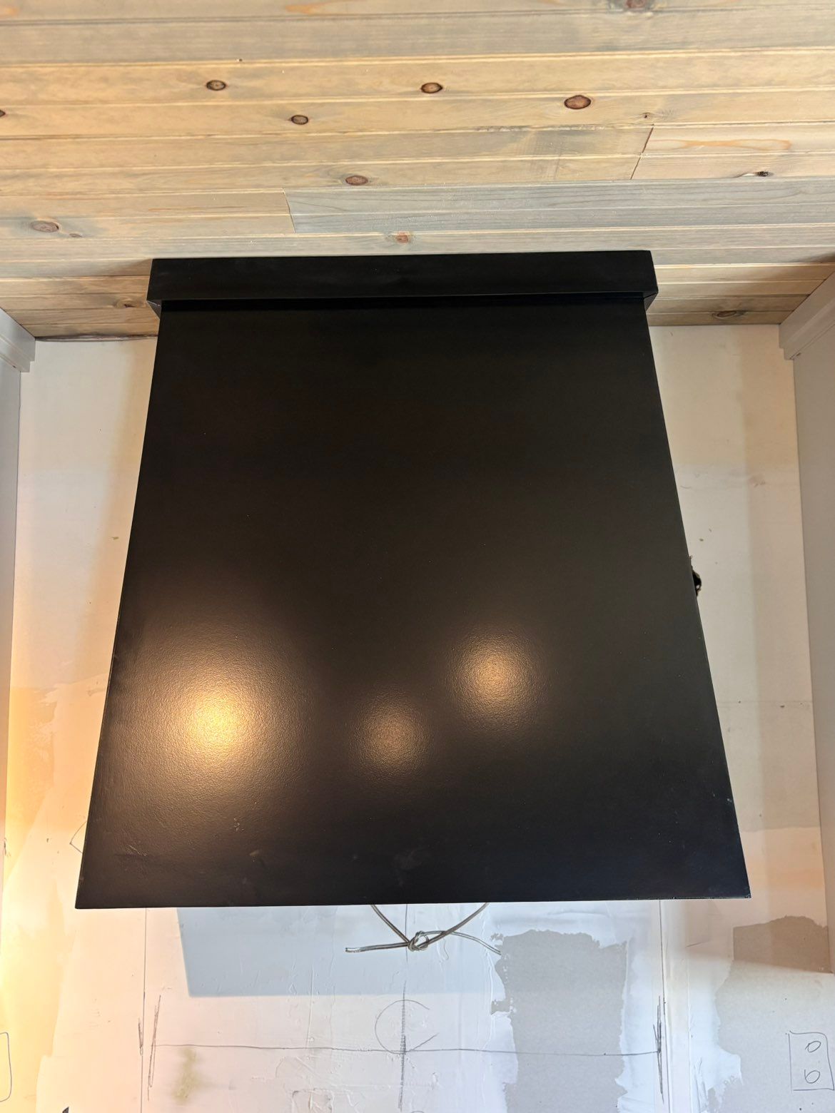 Black window shade covering a window in a white room with wood ceiling trim