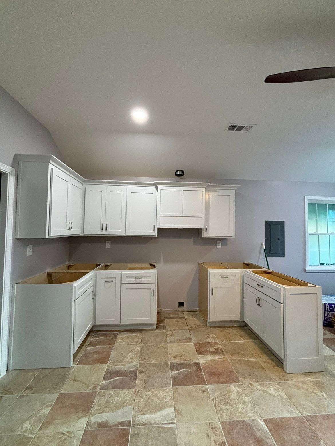Empty kitchen with white cabinets, beige tile floor, and a bright ceiling light in a small room.