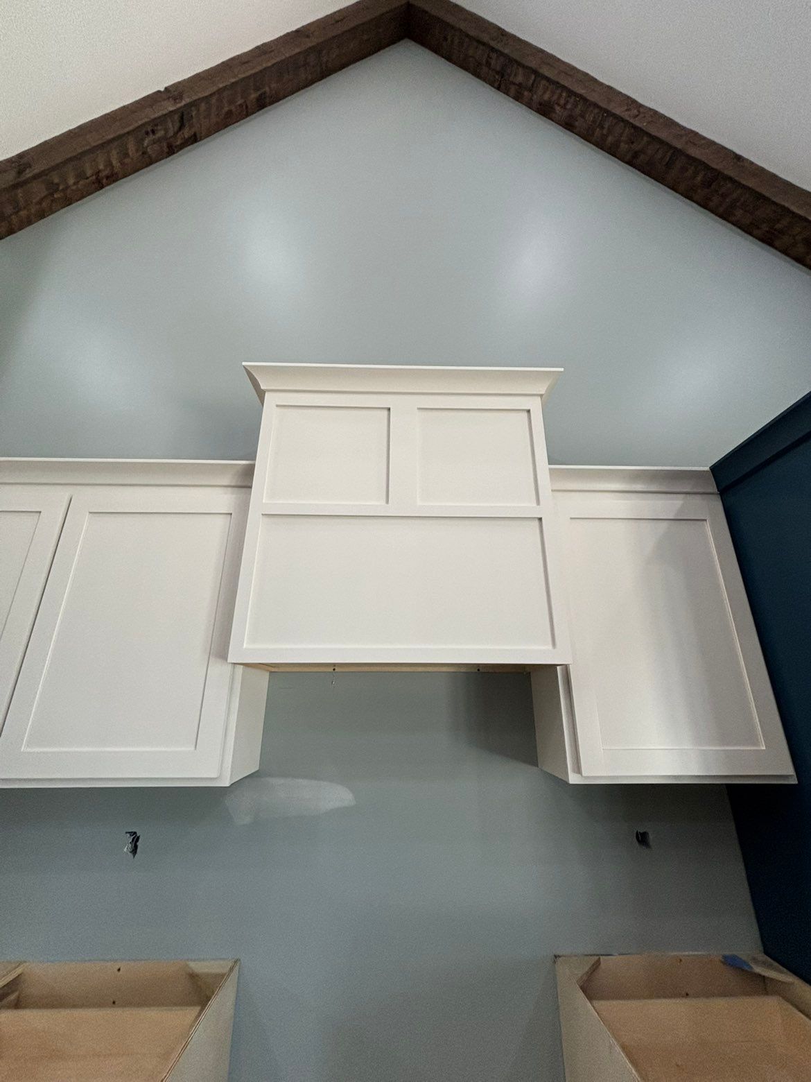 White kitchen cabinets mounted on a gray wall beneath a vaulted ceiling, with a center cabinet missing.