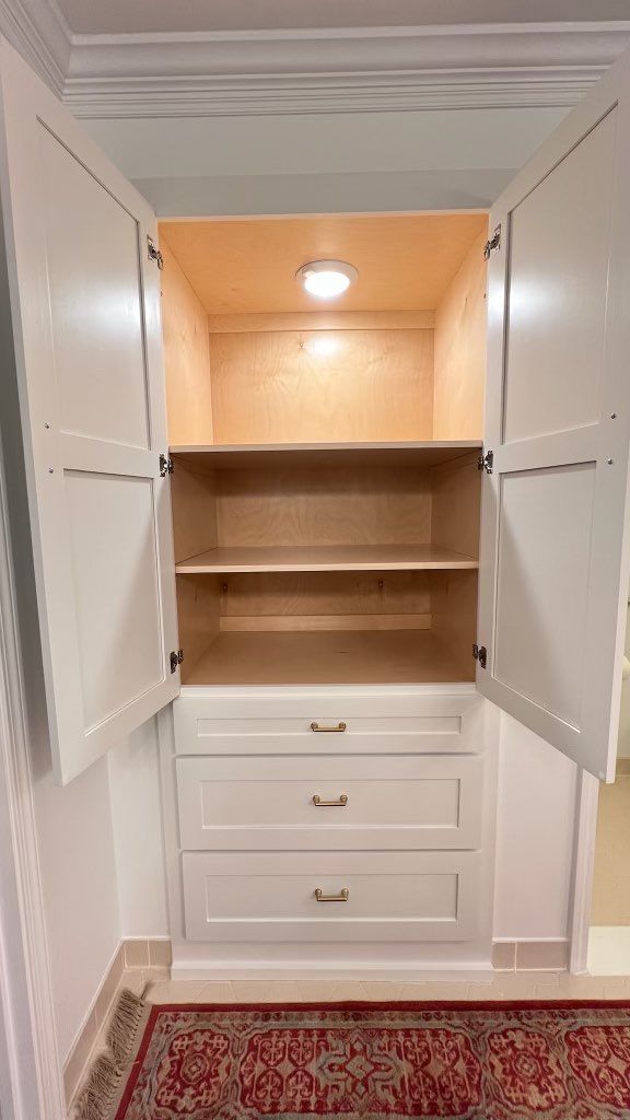 Open white built-in cabinet with shelves, drawers, and a recessed light above a red rug.
