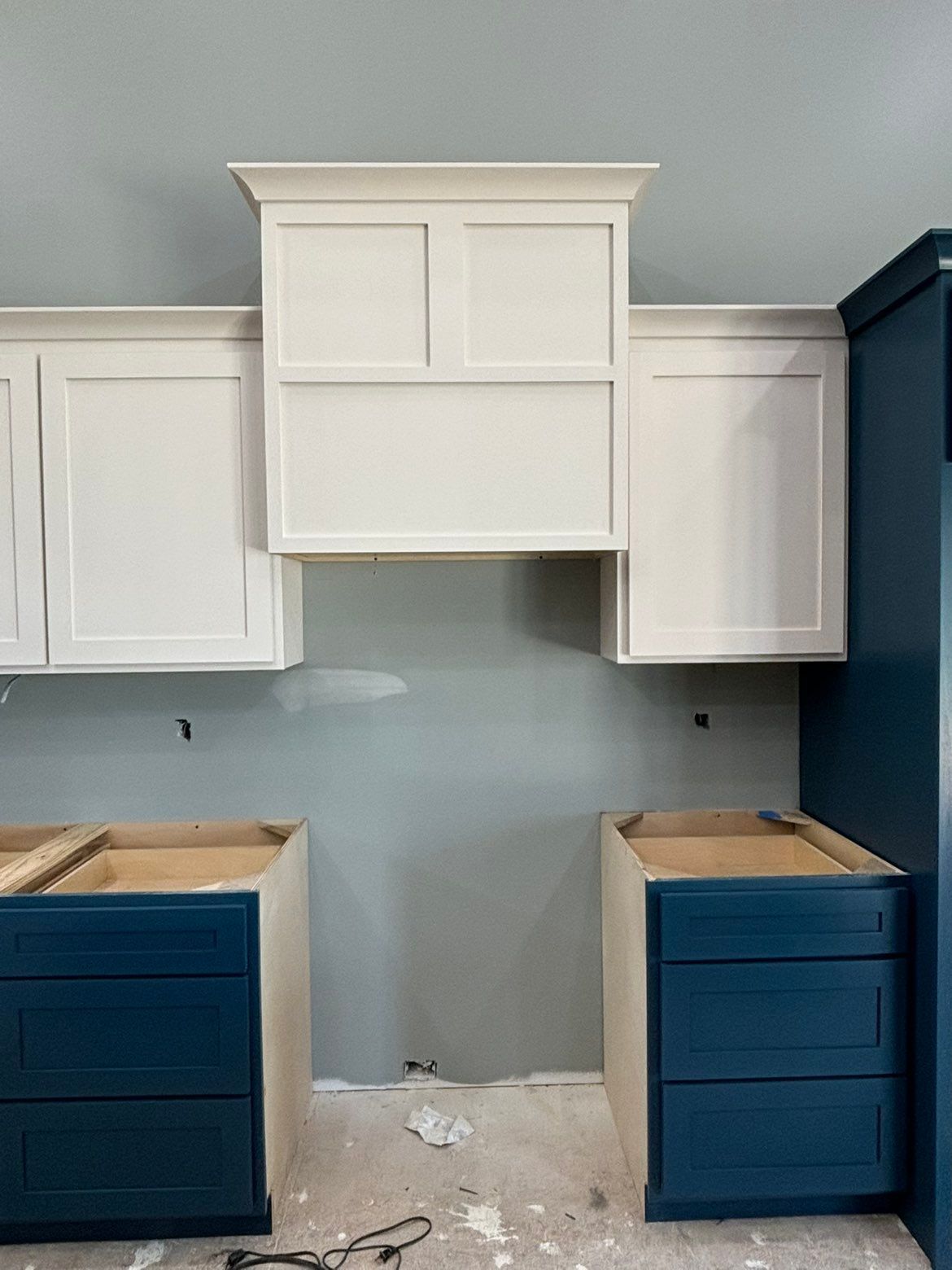 Kitchen under renovation with white upper cabinets, blue lower cabinets, and unfinished countertops and floor