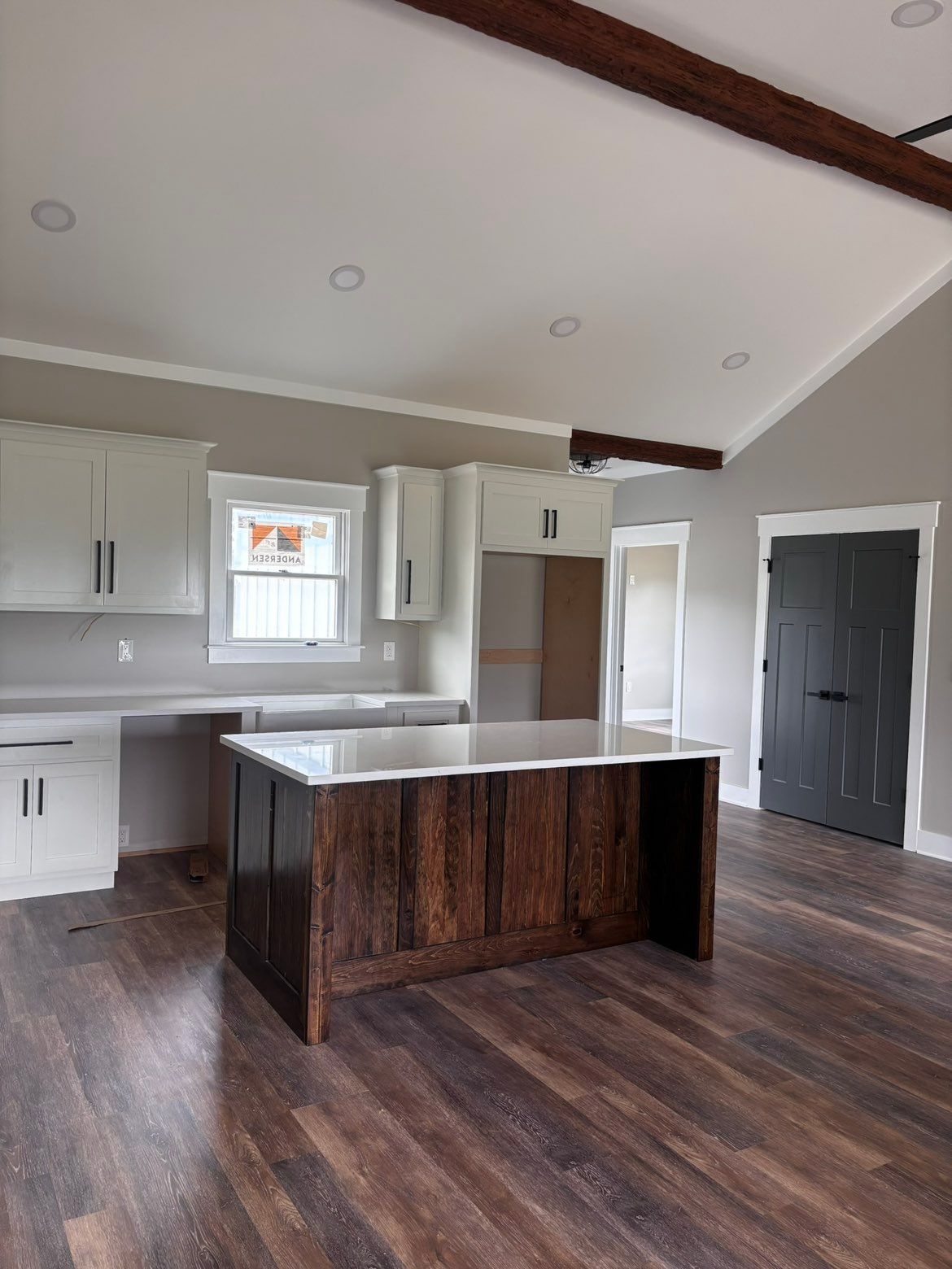 Empty modern kitchen with dark wood floors, white cabinets, and a central island under vaulted ceilings