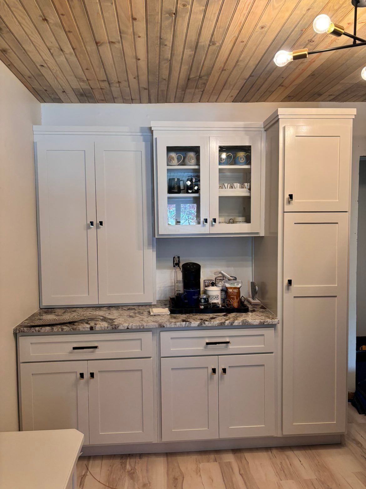 White kitchen cabinets with granite countertop, glass-front center cabinet, and wood plank ceiling