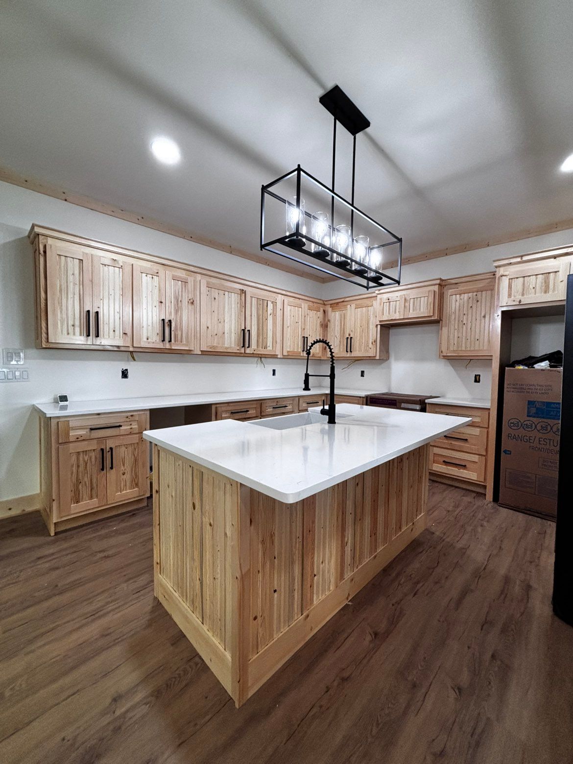 Spacious kitchen with light wood cabinets, large white island, black pendant light, and dark wood floor