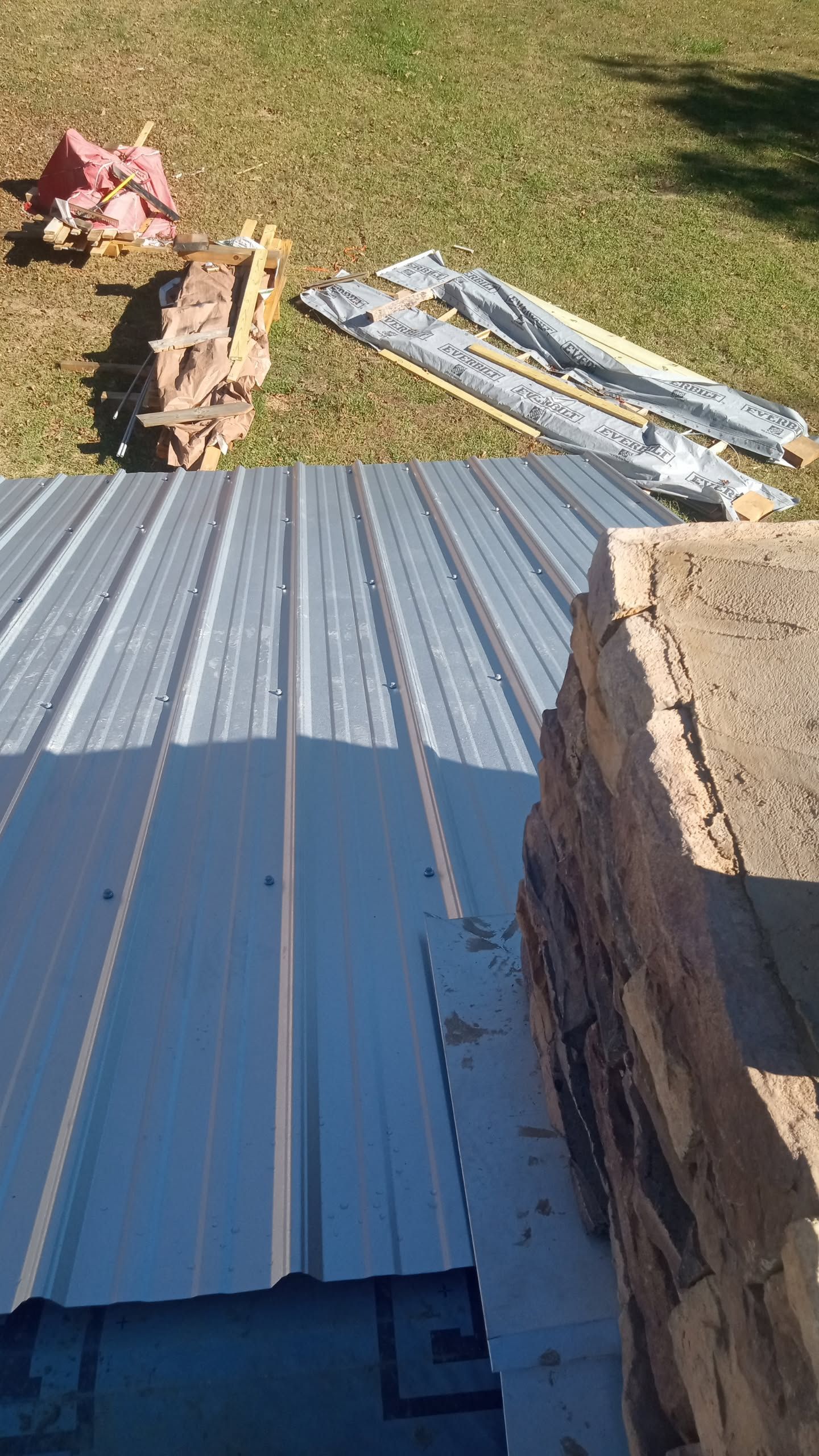 Corrugated metal roofing sheets on grass beside stacked bricks and a concrete block
