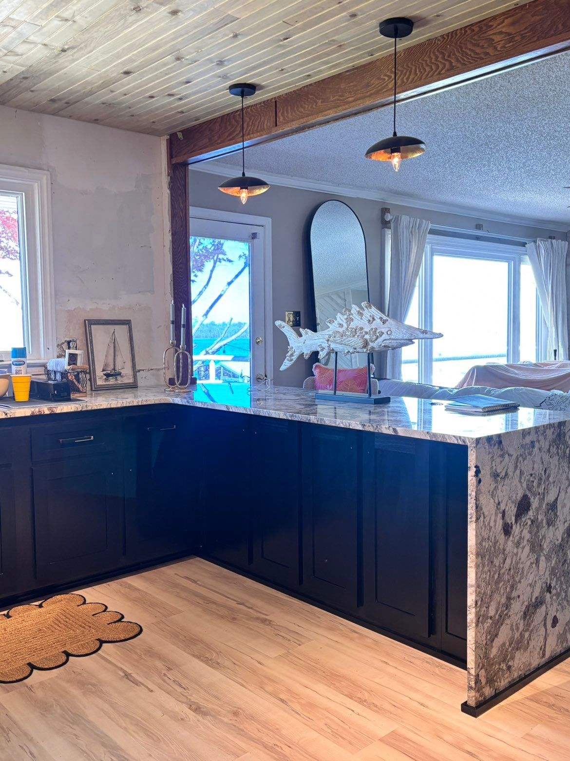 Modern kitchen with dark cabinets, stone island, pendant lights, and large windows.