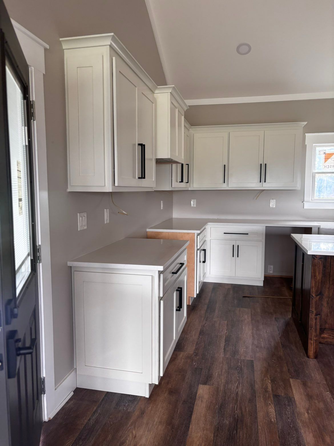 Compact kitchen with white cabinets, dark wood floor, and a large window over the counter.