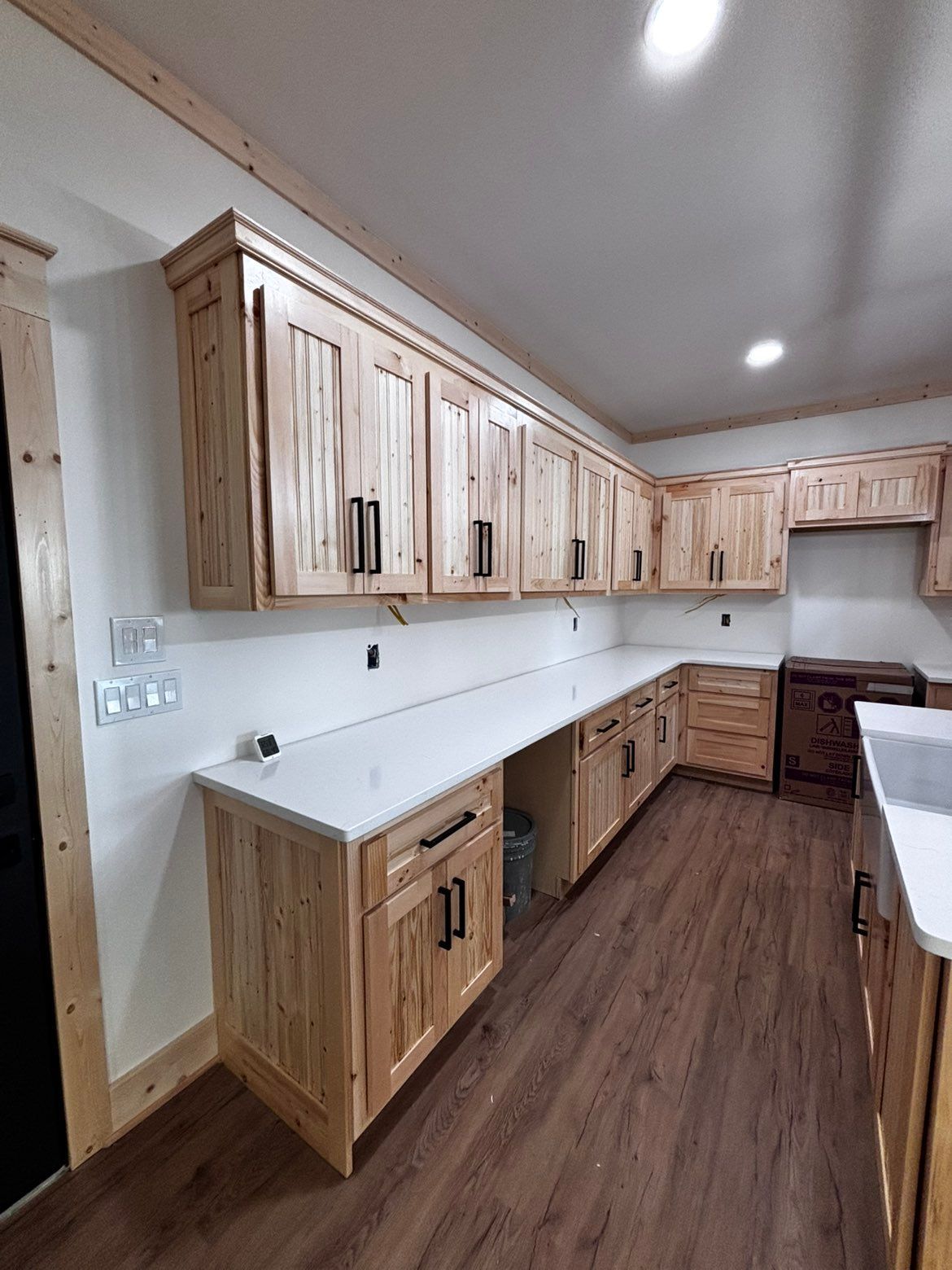 Bright kitchen with light wood cabinets, white countertops, and dark wood flooring.