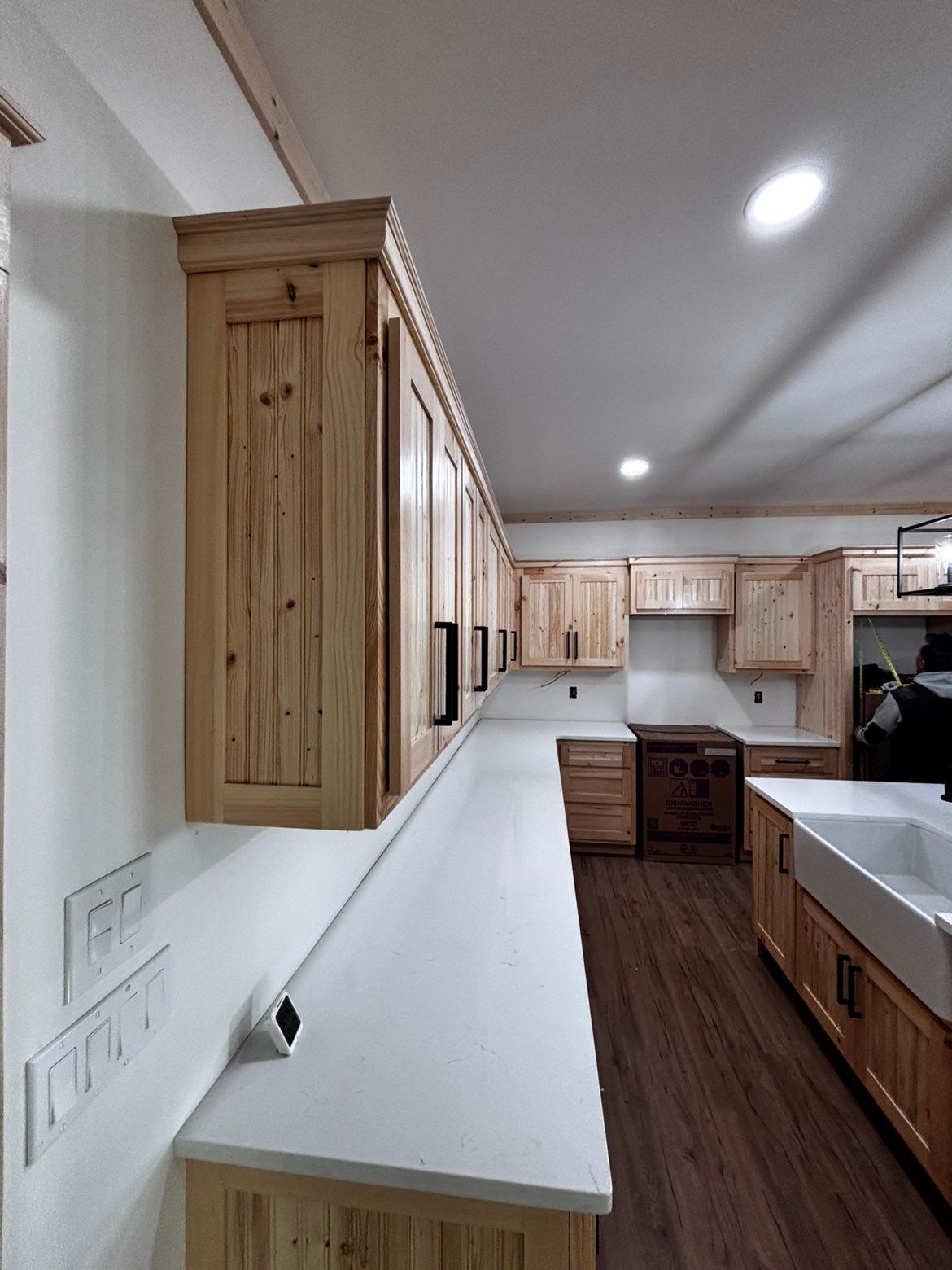 Long narrow kitchen with light wood cabinets, white counters, and dark wood flooring
