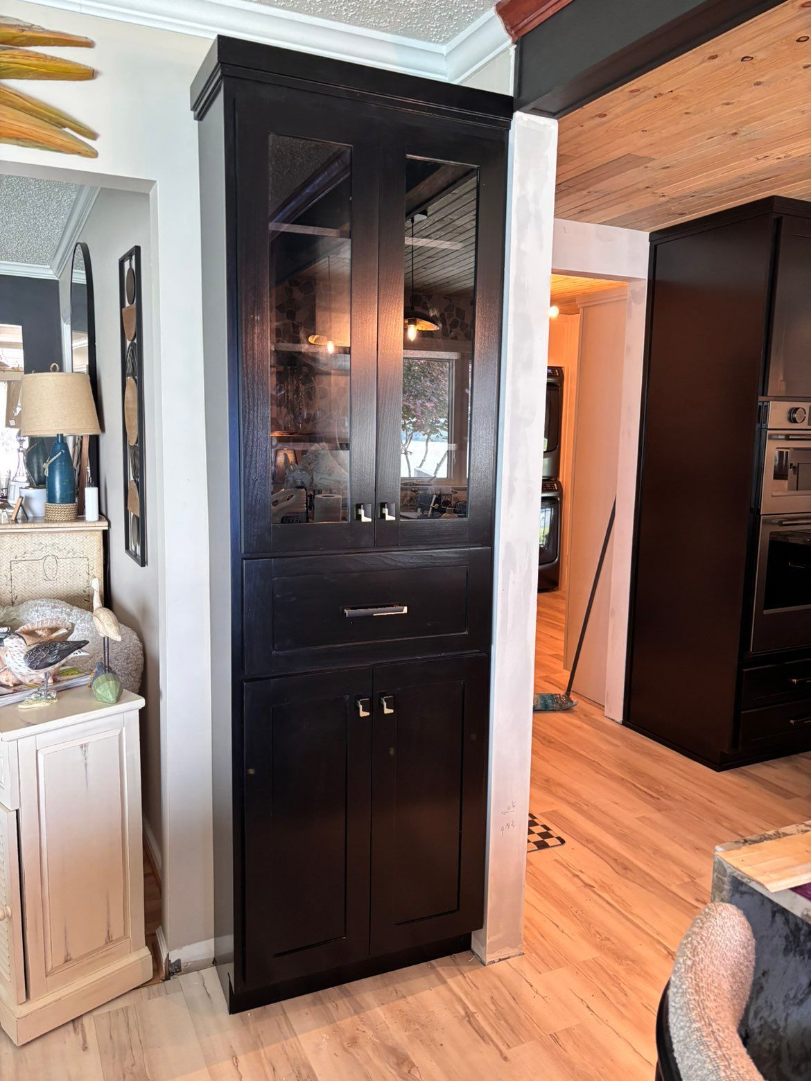 Tall black display cabinet with glass doors in a bright living room beside a white sideboard.
