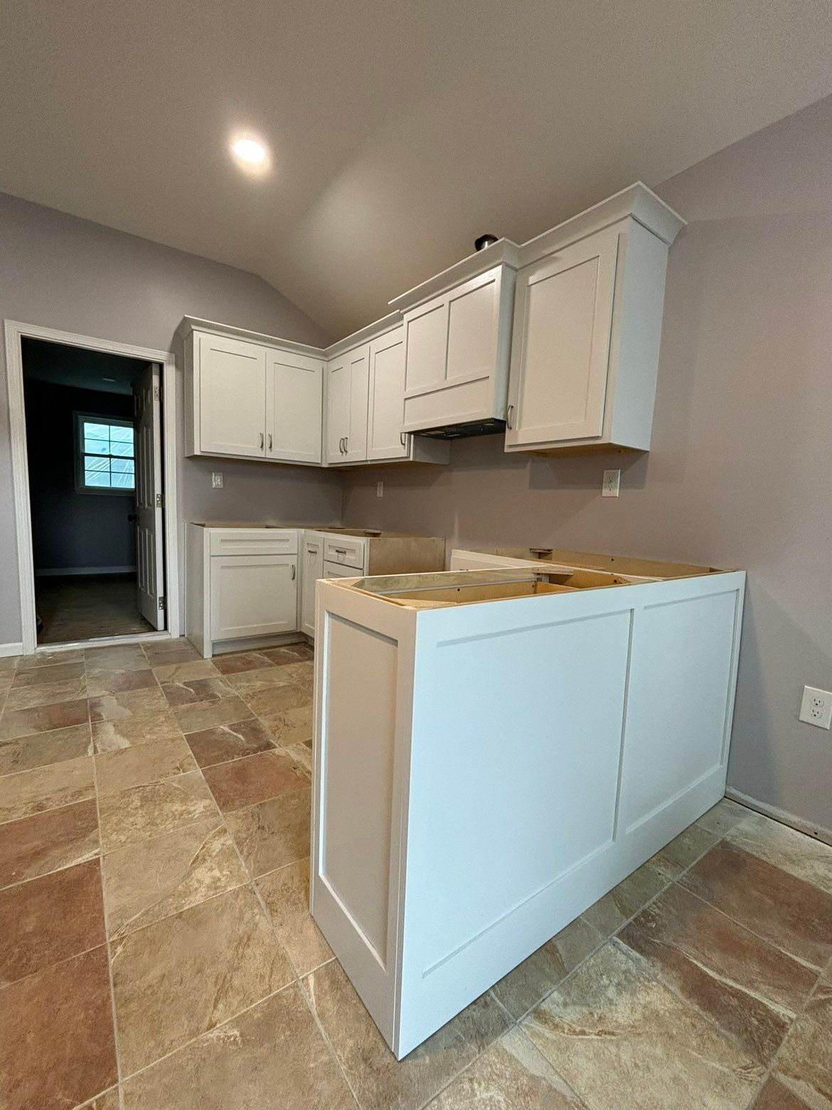 Empty kitchen under renovation with white cabinets, tiled floor, and a half-finished island.