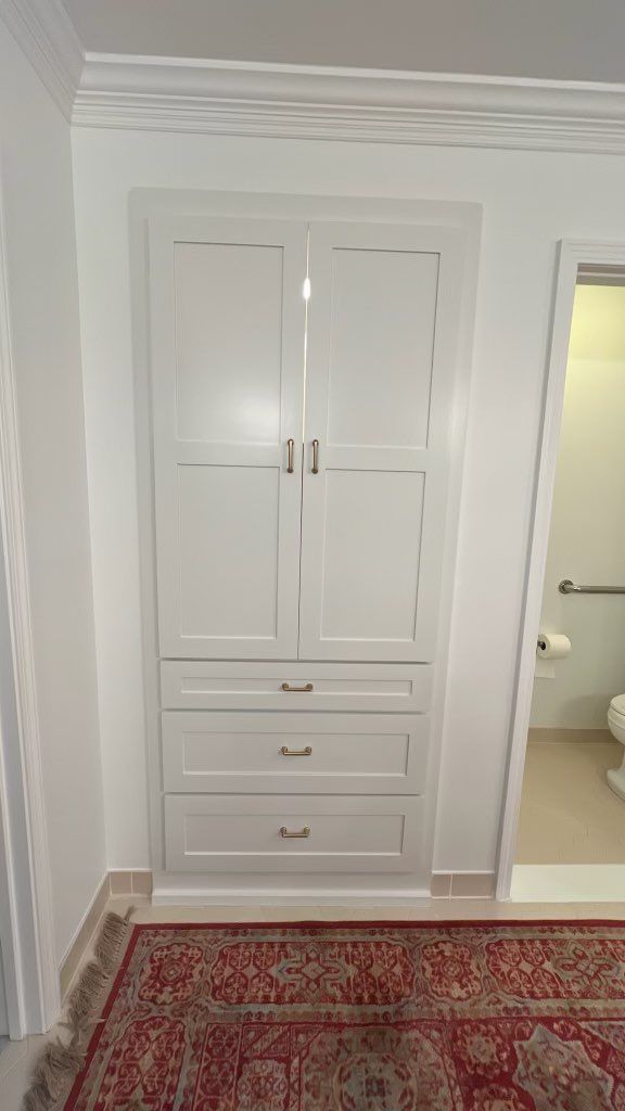 Built-in white cabinet with drawers and doors in a bright hallway, beside a doorway and red patterned rug
