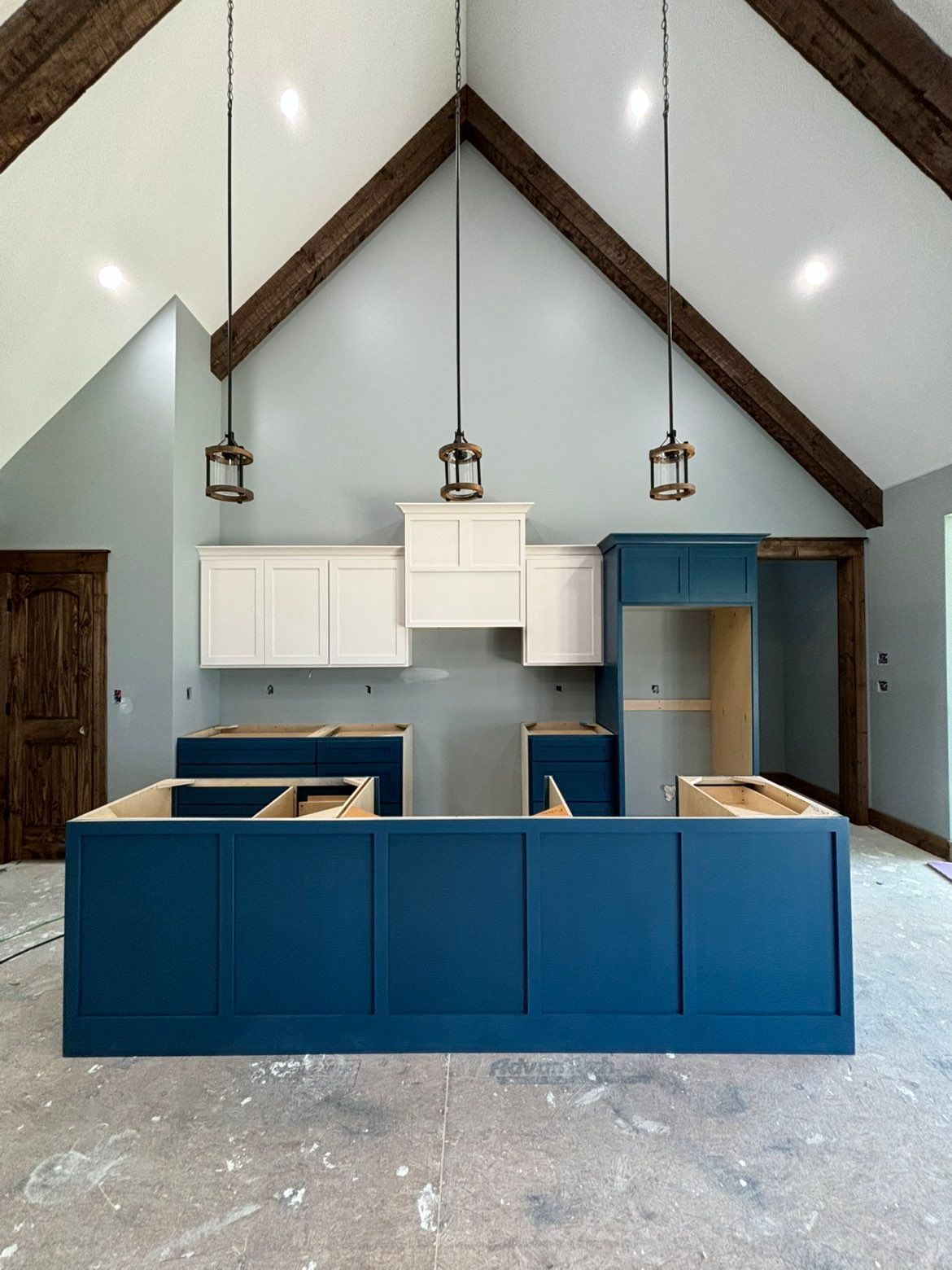 Bright blue kitchen island in a vaulted room with white cabinets and hanging pendant lights