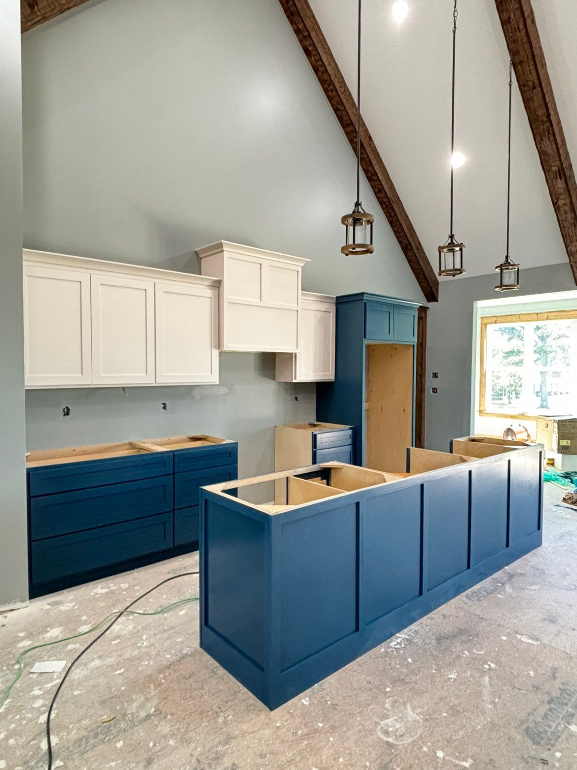 Modern kitchen under construction with blue island, white cabinets, and exposed beams
