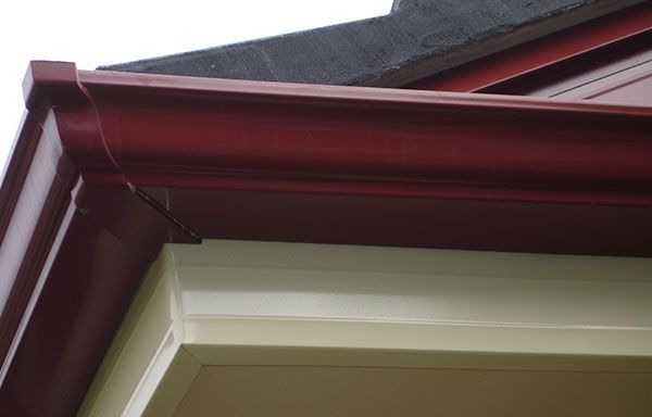 Close-up of a house roof eave with dark red trim and beige siding under gray shingles