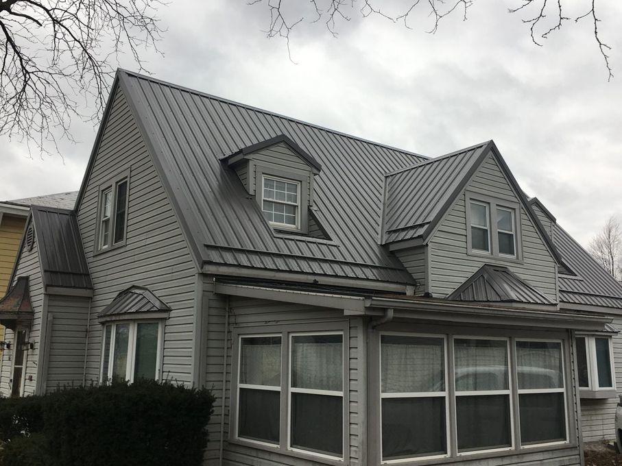 Gray shingled house with steep roof and large front windows under an overcast sky
