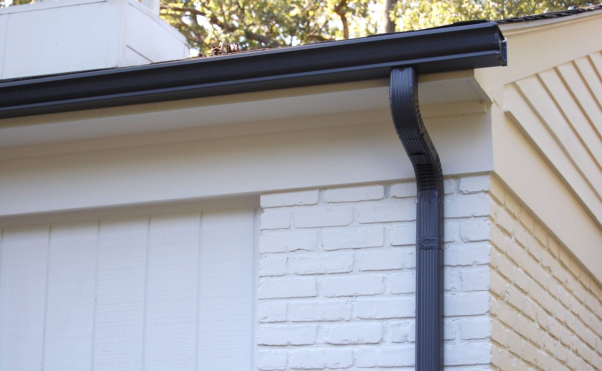White house eave with black gutter and downspout against white brick siding