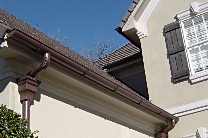 House roof and eaves against a clear blue sky, with a white window shutter and brown guttering.