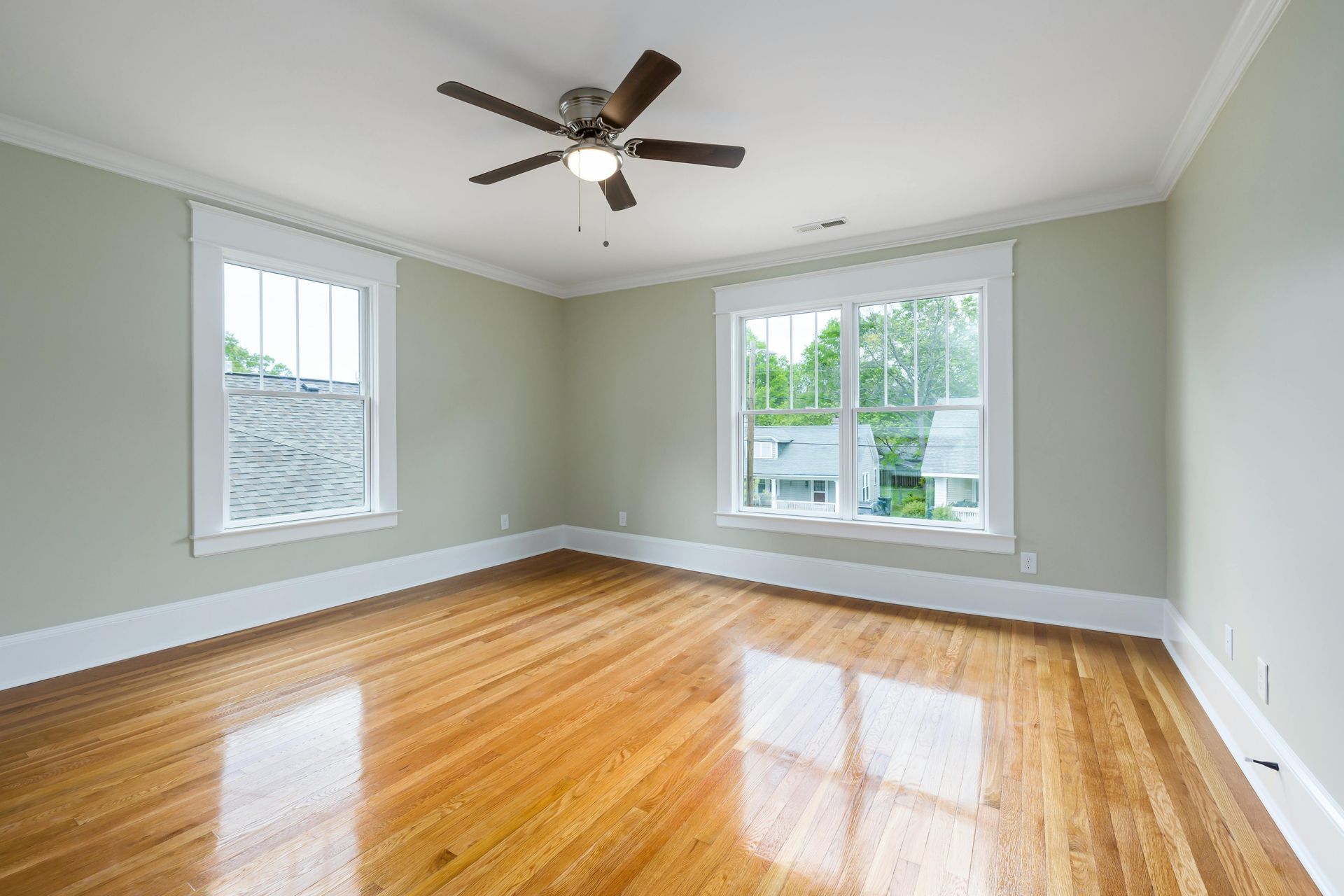 Bright empty room with hardwood floors, gray walls, two windows, and a ceiling fan
