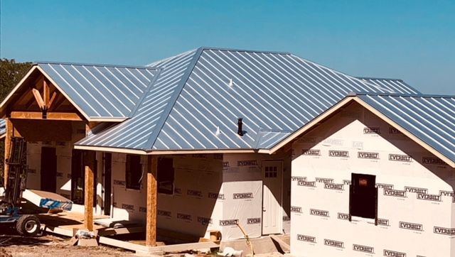 Partially built house with gray metal roof and white exterior walls at a construction site