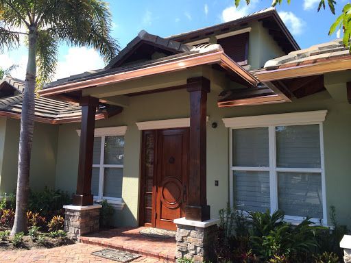 Front entrance of a house with a wooden door, white shutters, and a covered porch with columns