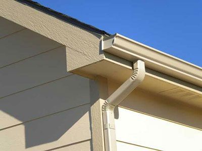 Close-up of beige house eaves with a white rain gutter and downspout against a blue sky
