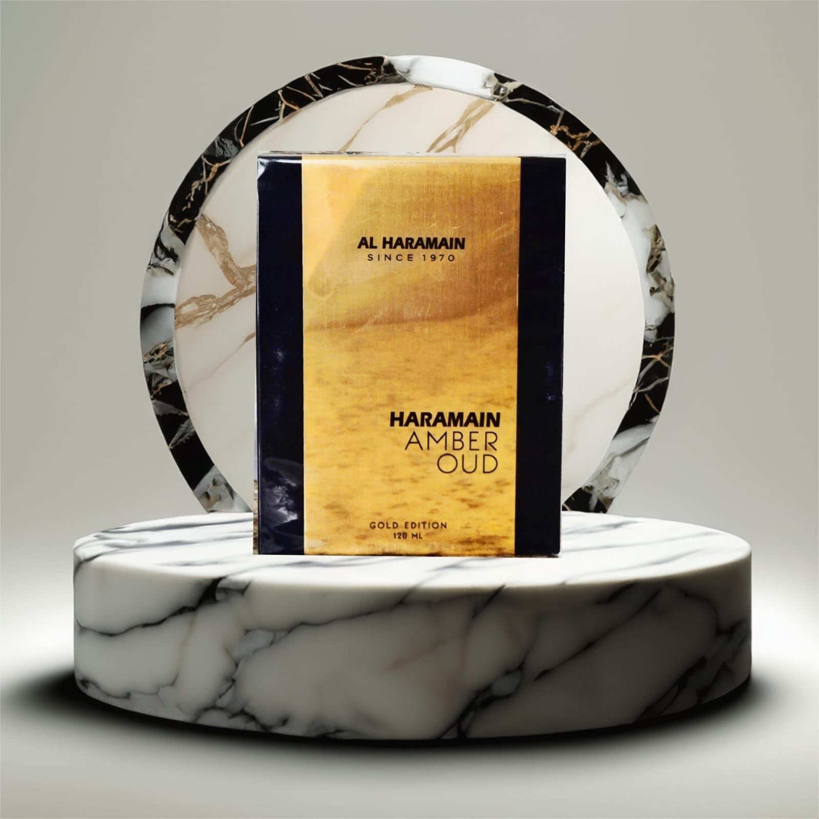 Caja de perfume Al Haramain Amber Oud sobre un pedestal de mármol, frente a un anillo de mármol negro.