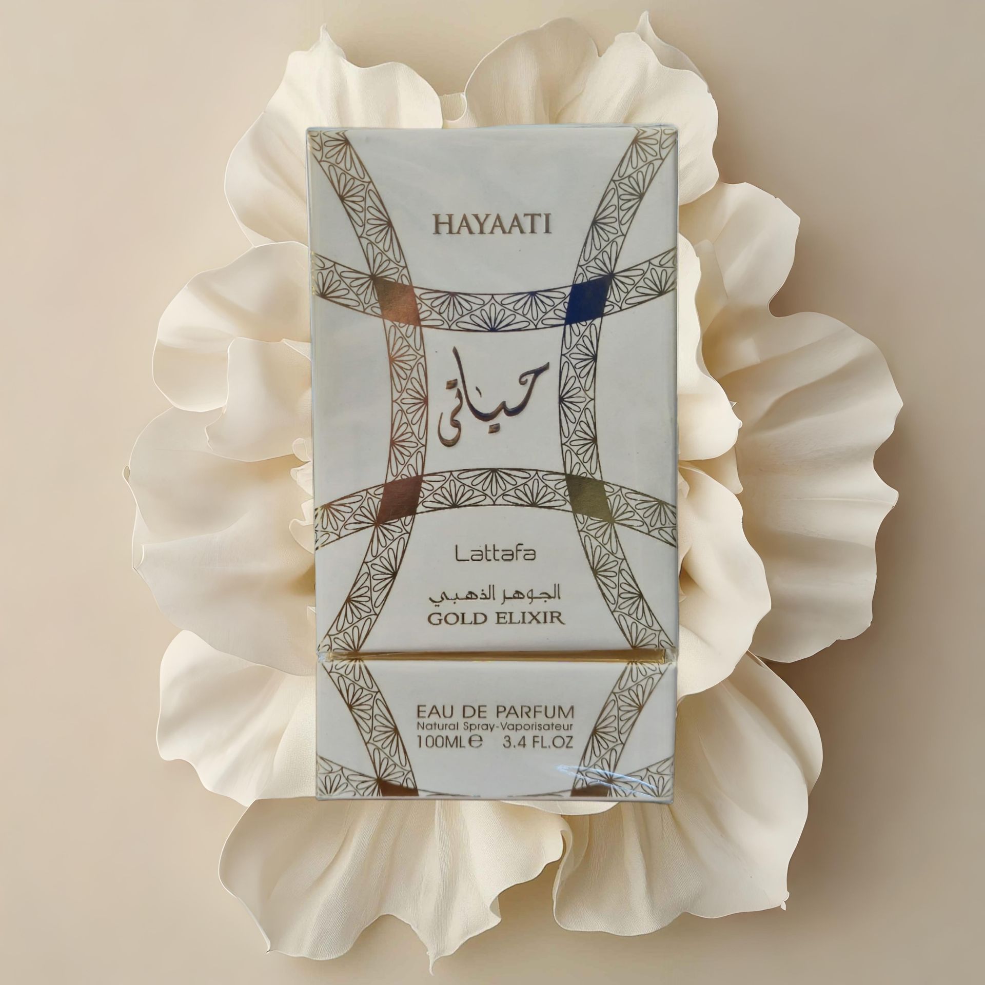 La caja de perfume blanca, "Hayaati Gold Elixir", reposa sobre un lecho de pétalos de flores de color blanco cremoso.