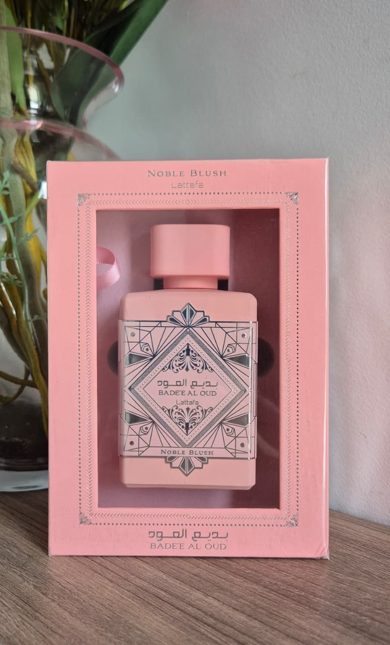 Frasco de perfume rosa sobre un pedestal redondo rodeado de flores.