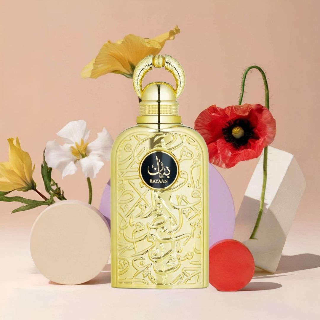 Frasco de perfume dorado con detalles ornamentados, rodeado de flores y formas geométricas sobre un fondo melocotón.