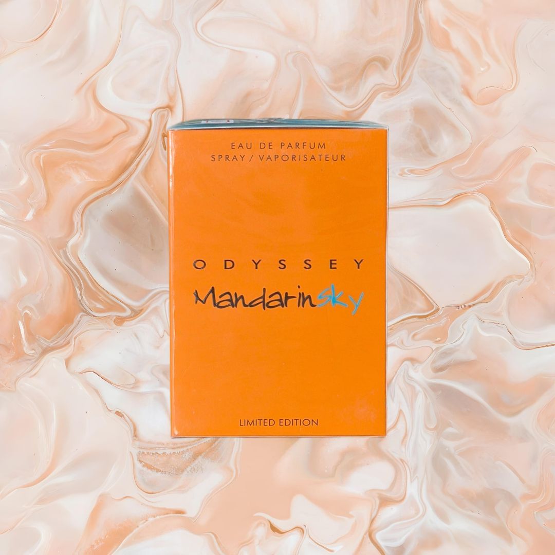 Una caja naranja del perfume “Odyssey Mandarin Sky” sobre un fondo color melocotón jaspeado.