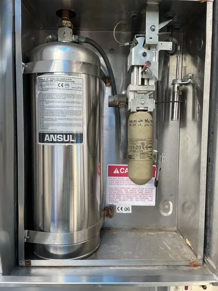 A stainless steel fire extinguisher is sitting inside of a metal box.