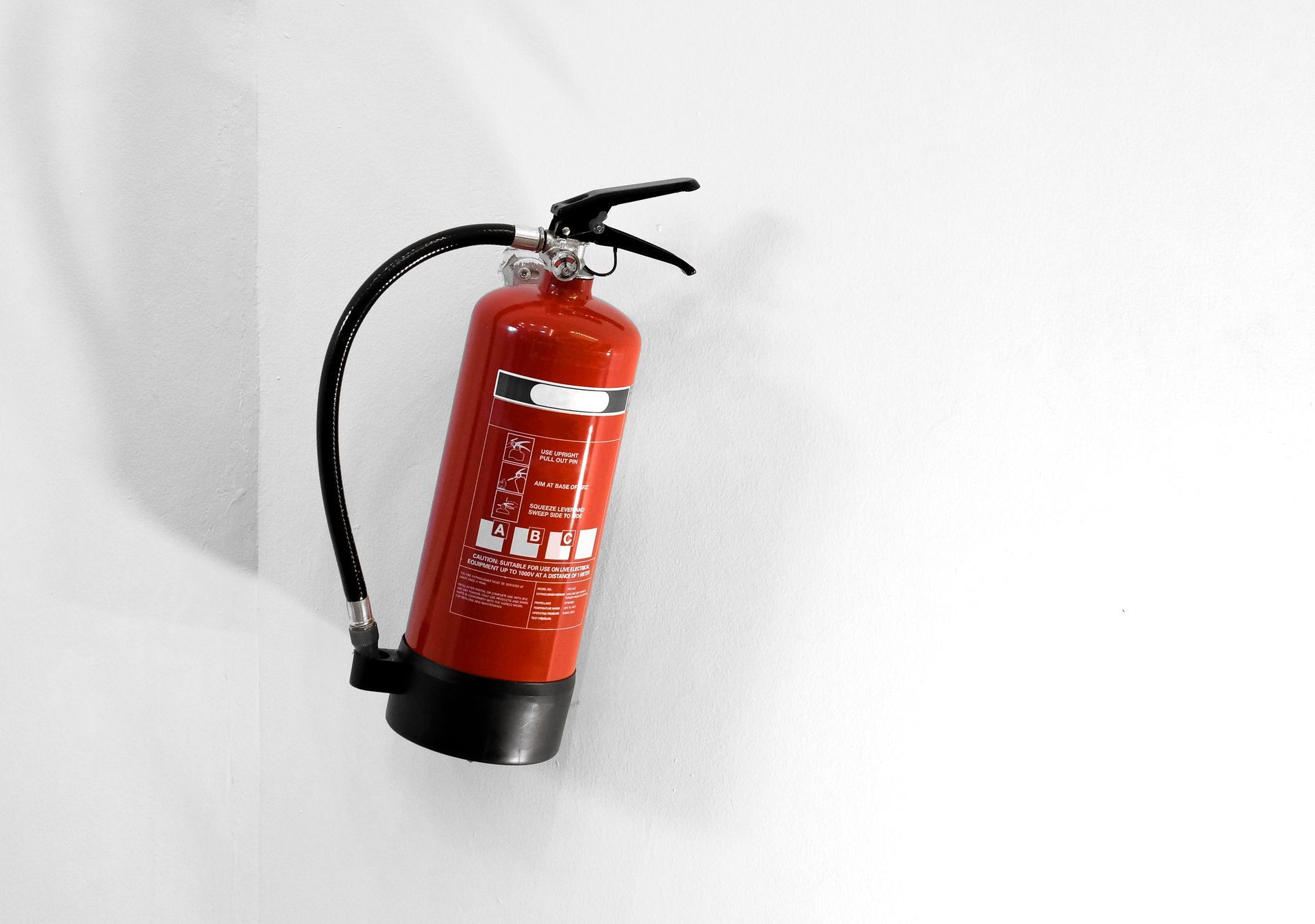 A red fire extinguisher is hanging on a white wall.