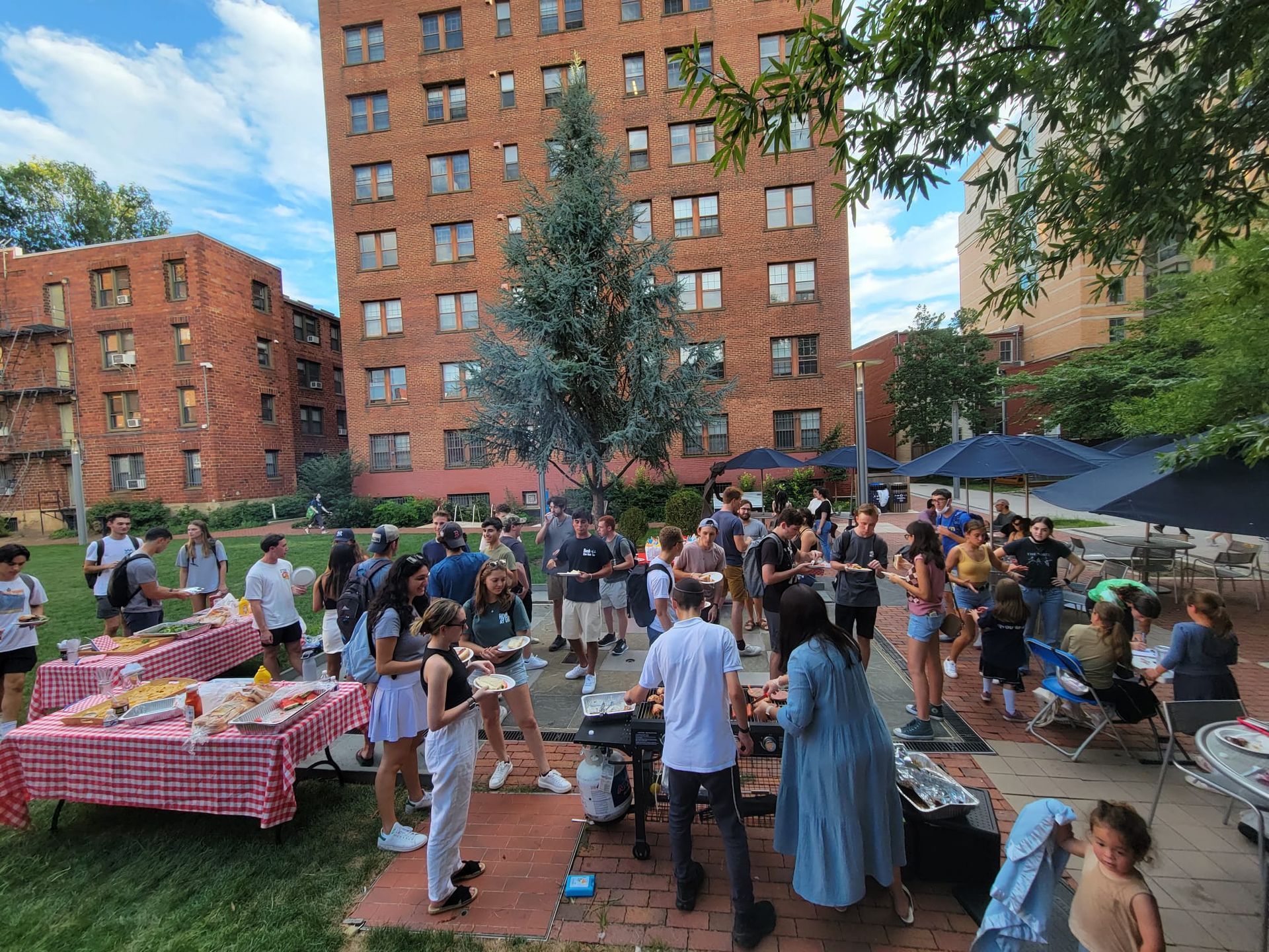 A large group of people are standing around tables in a park.