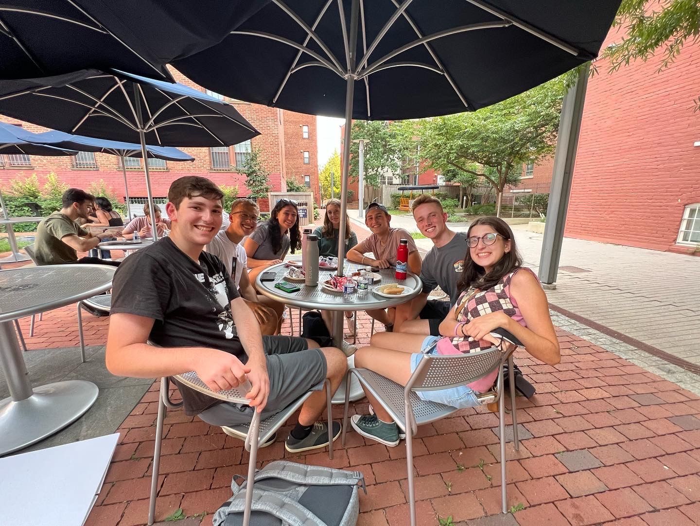 a group of people are sitting at tables under umbrellas .