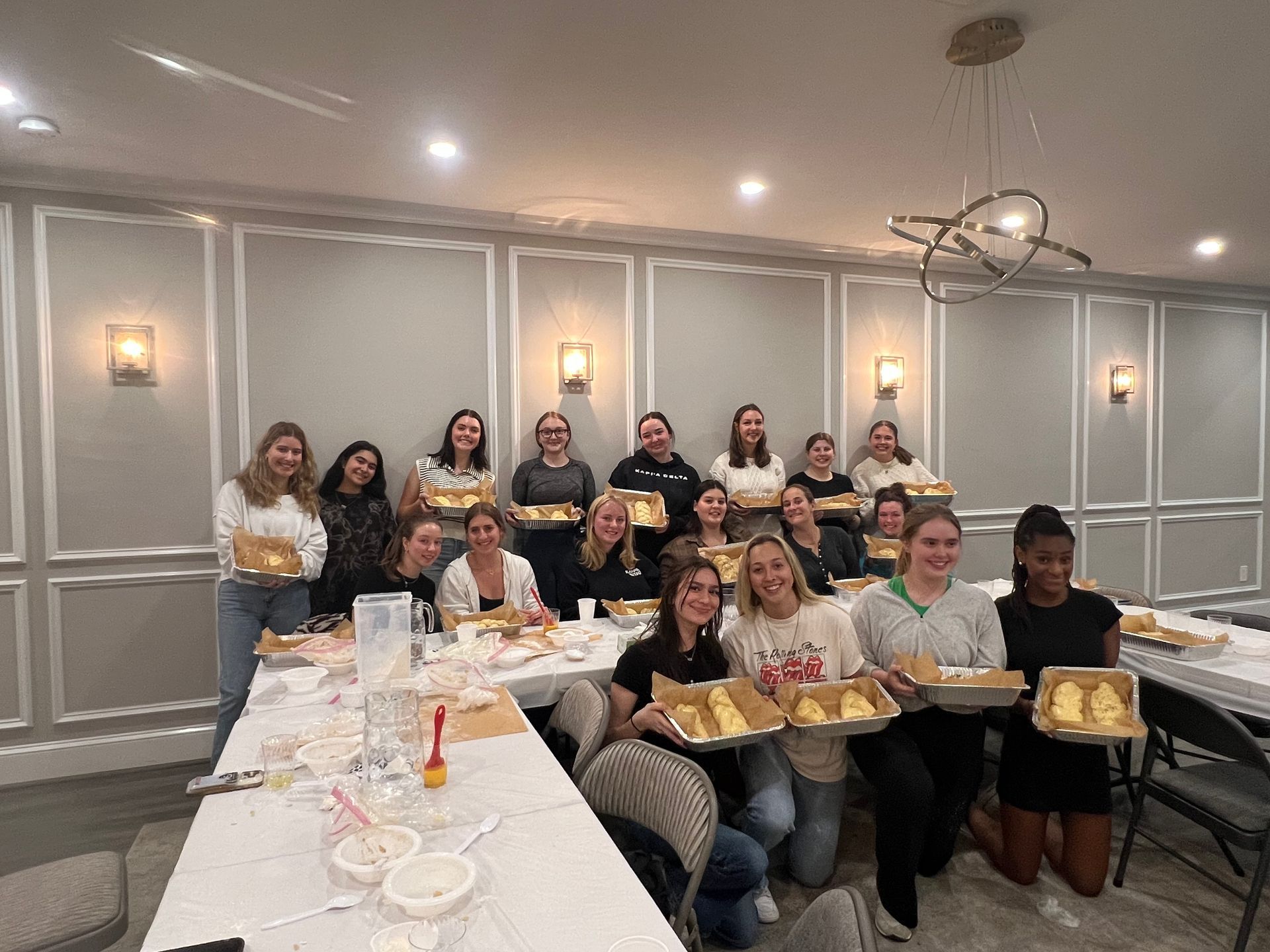 A group of women are sitting at a long table holding trays of food.